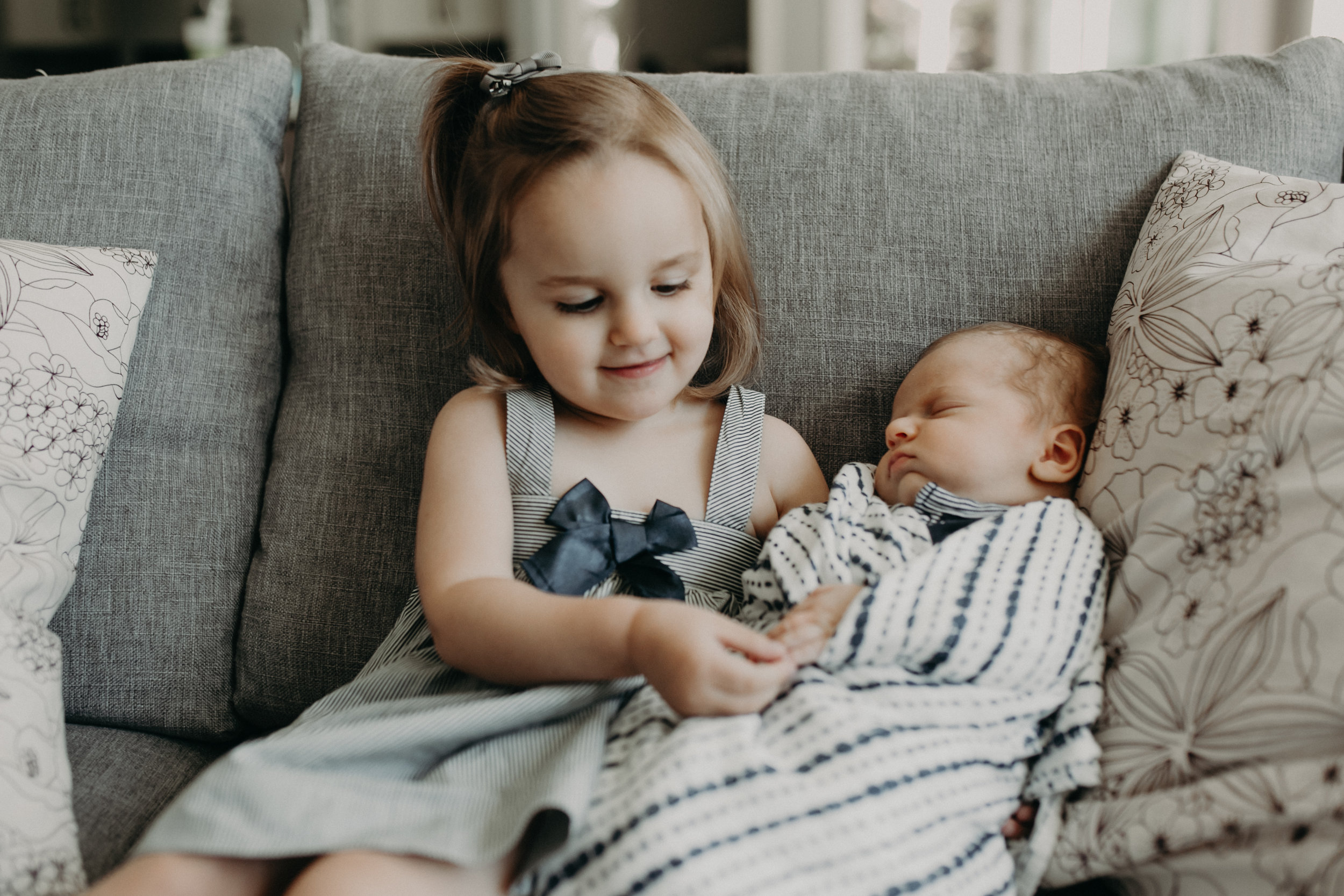  big sister playing with newborn brother’s hands 