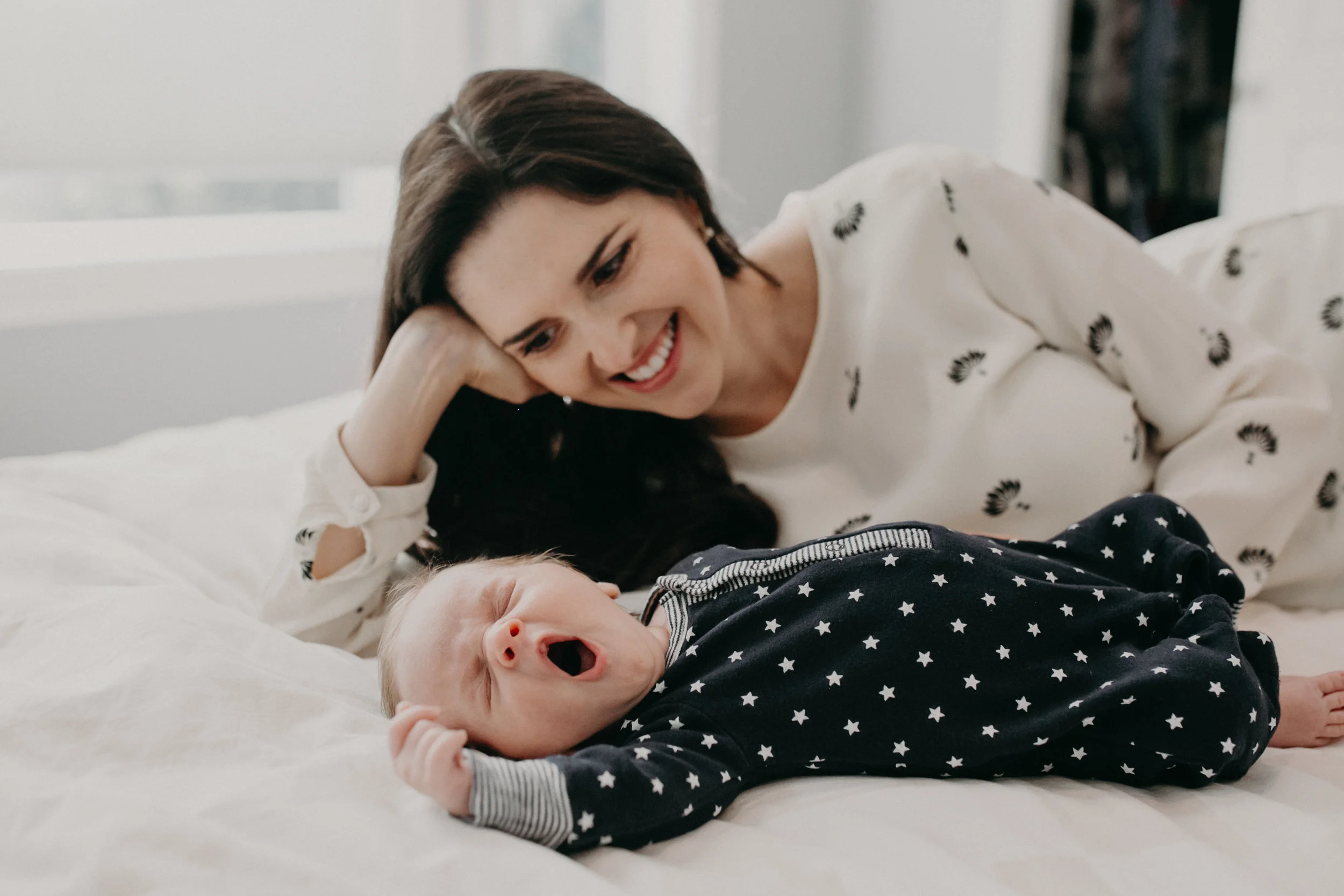 baby boy yawning while mom lays with him on bed in lifestyle newborn session with Andrea Wagner Photography