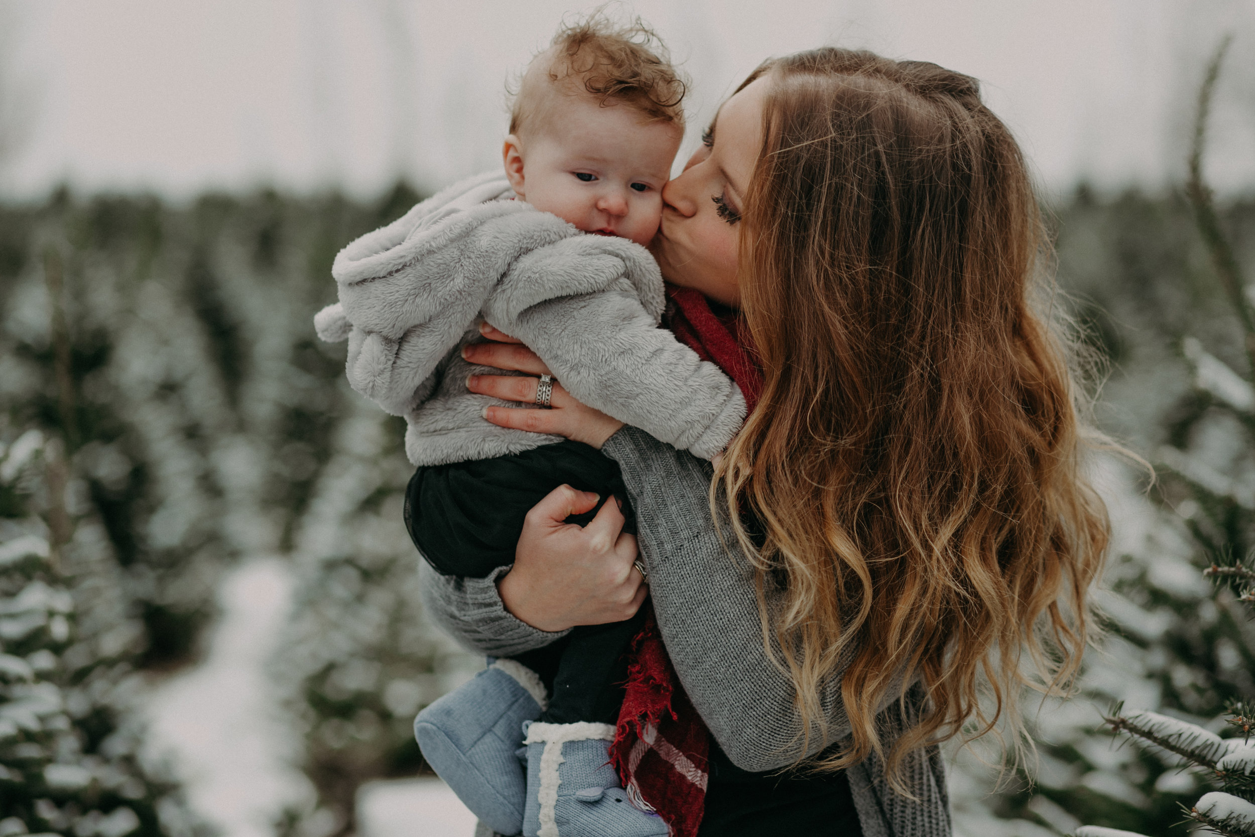  mommy kissing 6 month old daughter during family photo session at Santa’s Evergreens in Hudson WI 