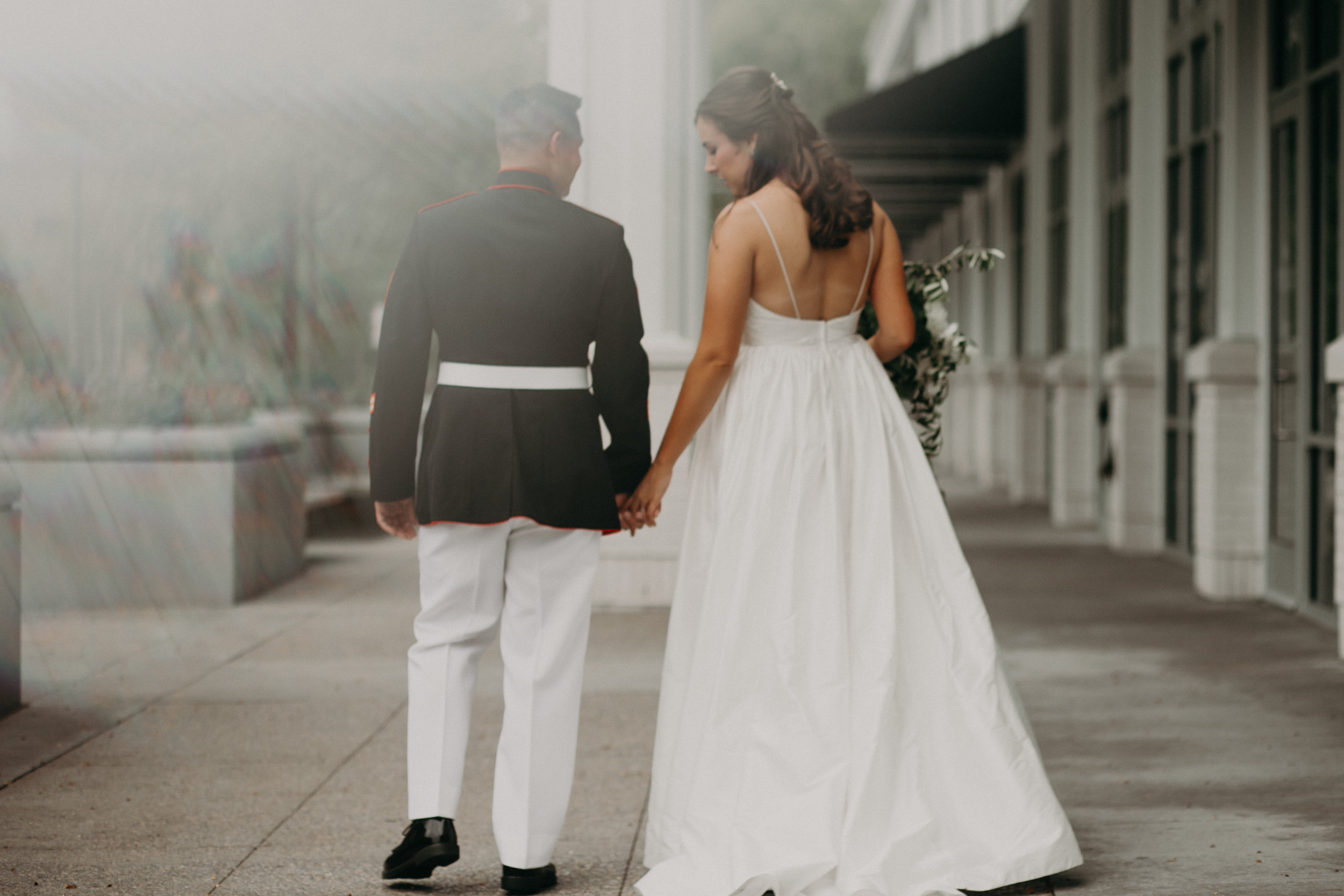 bride and military groom hold hands in front of Hotel Landing in Wayzata MN before their lake side wedding by Lake Minnetonka