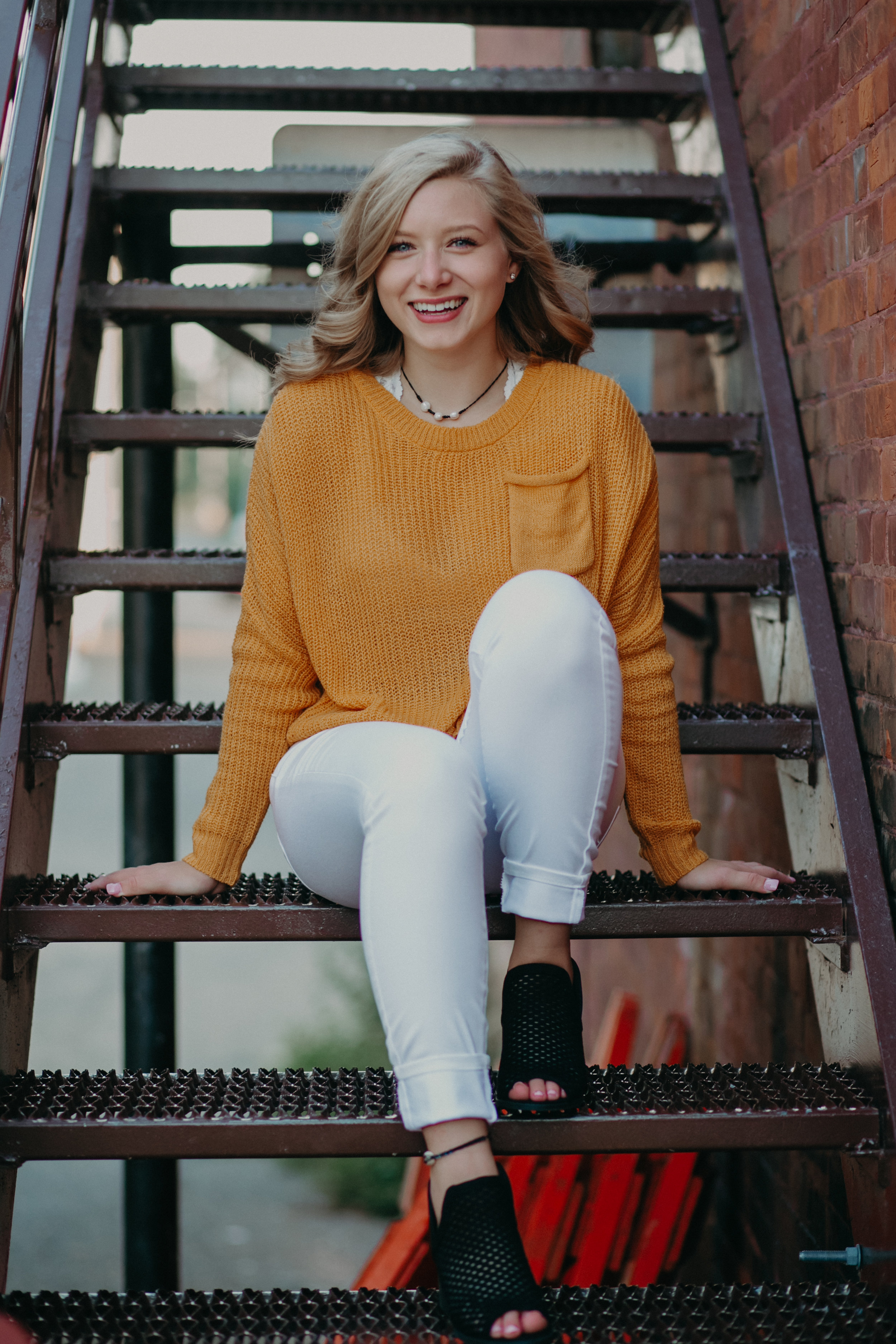 smiling senior sitting on steps in Hudson WI wearing a yellow sweater