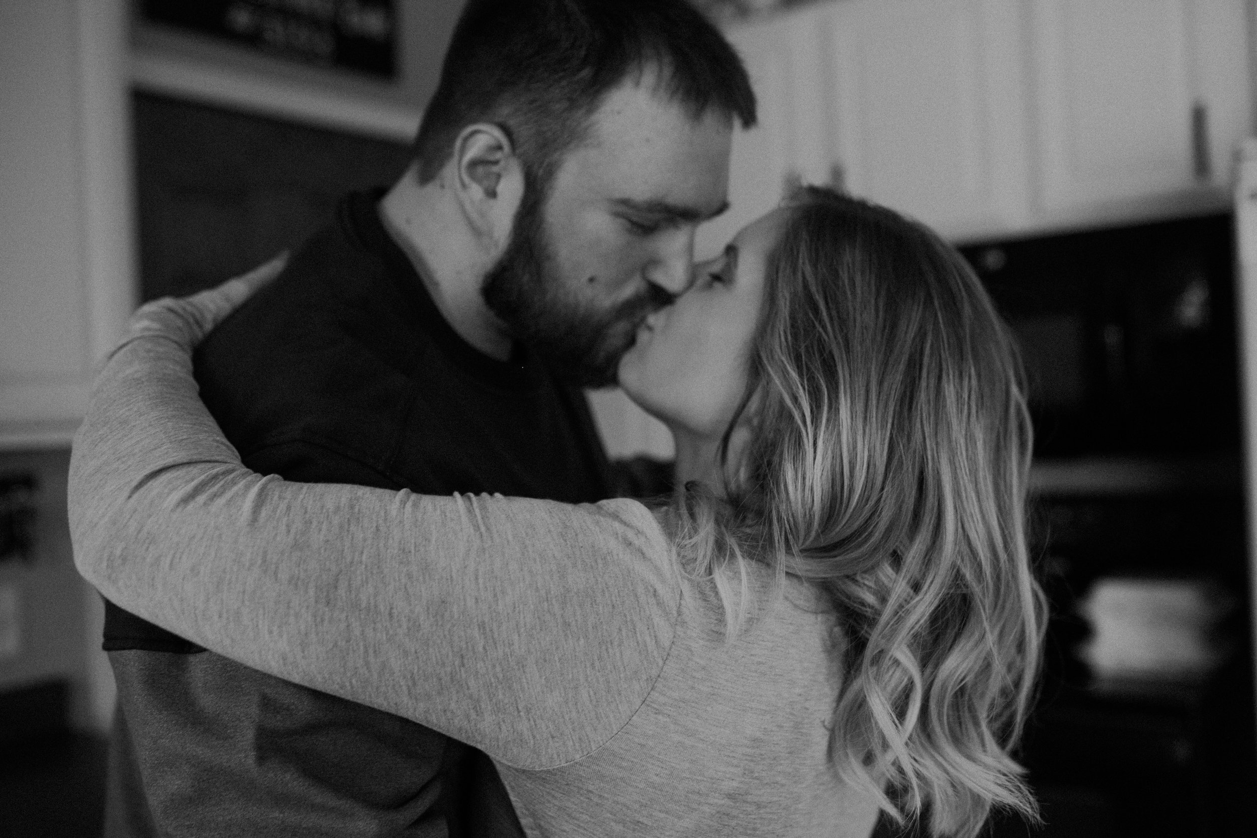  black and white photo of an engaged couple in their home kissing in the kitchen 