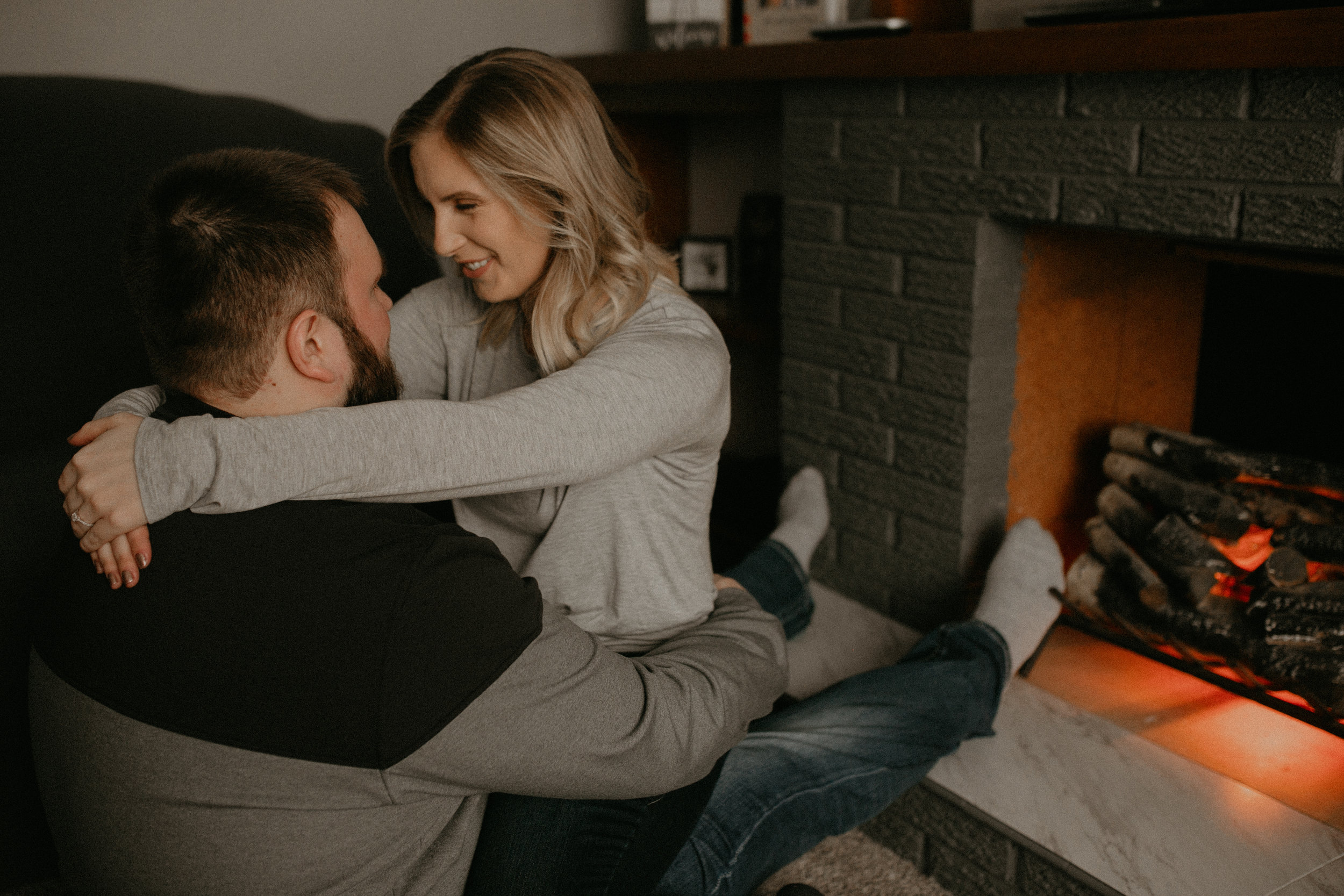  couple cozies up and snuggles near fireplace during lifestyle engagement session 