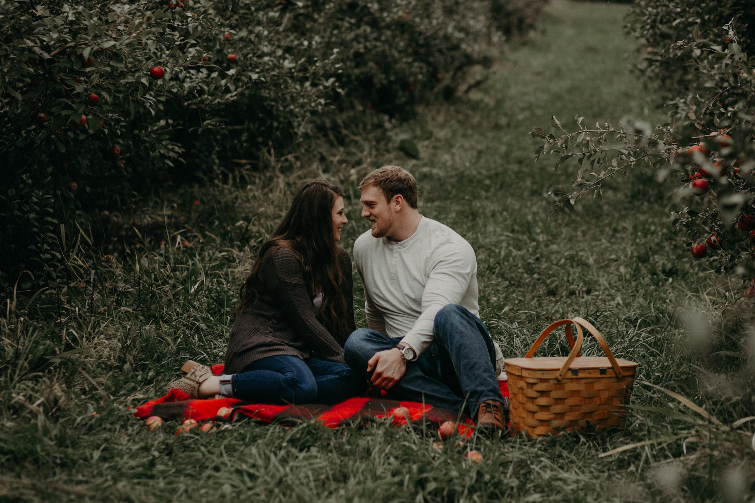  An engaged couple sits on a plaid blanket snuggling at Whistling Well Farm in Hastings MN 