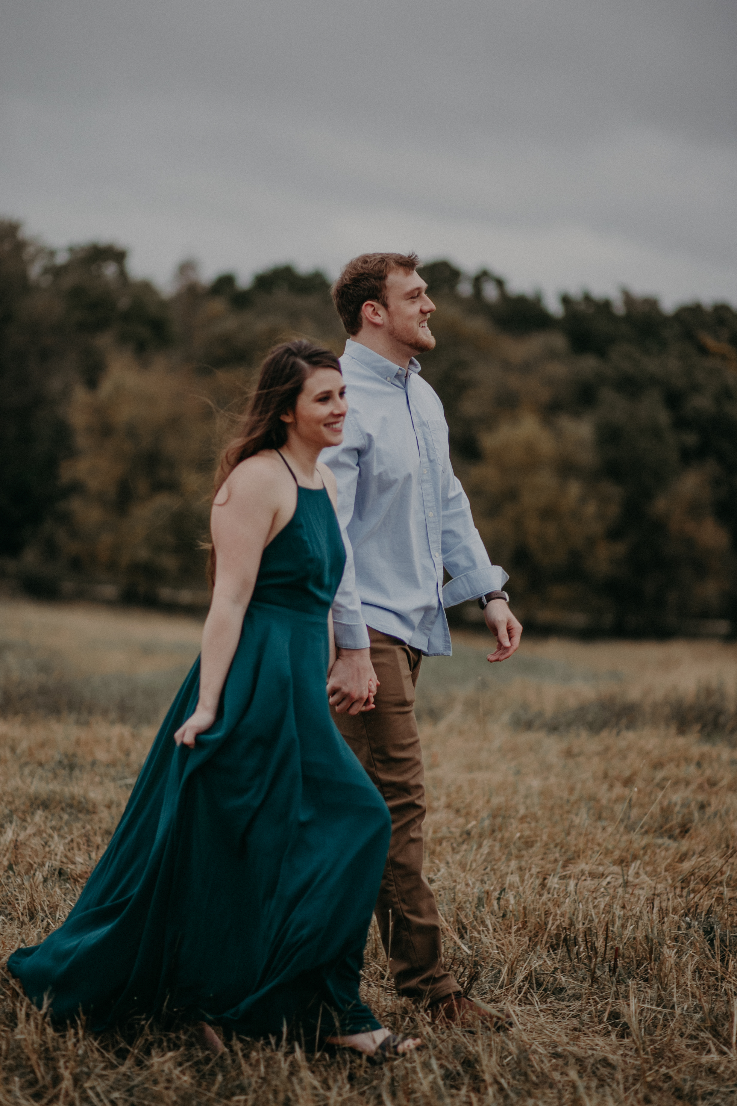A woman in a green dress walks with her fiancé through a meadow at sunset in Hastings MN