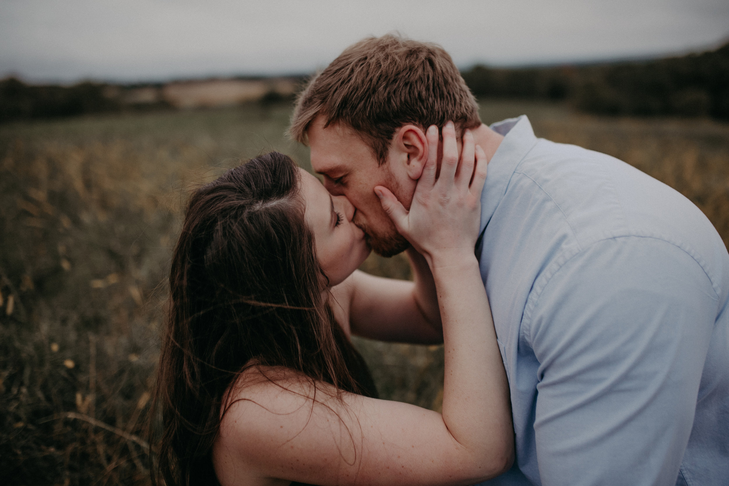A woman in a meadow kisses her fiancé romantically during a Minnesota engagement session
