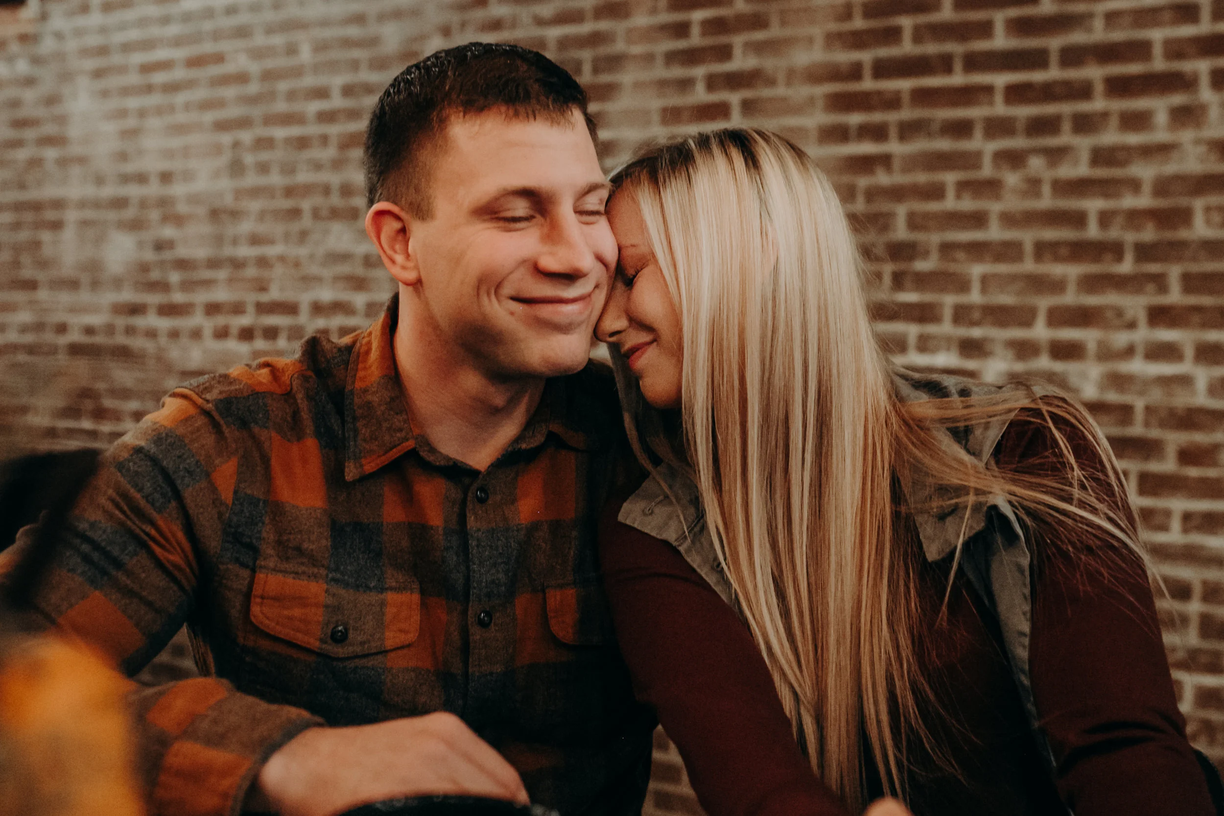 a man smiles while his fiancé snuggles him during an engagement session with Andrea Wagner Photography