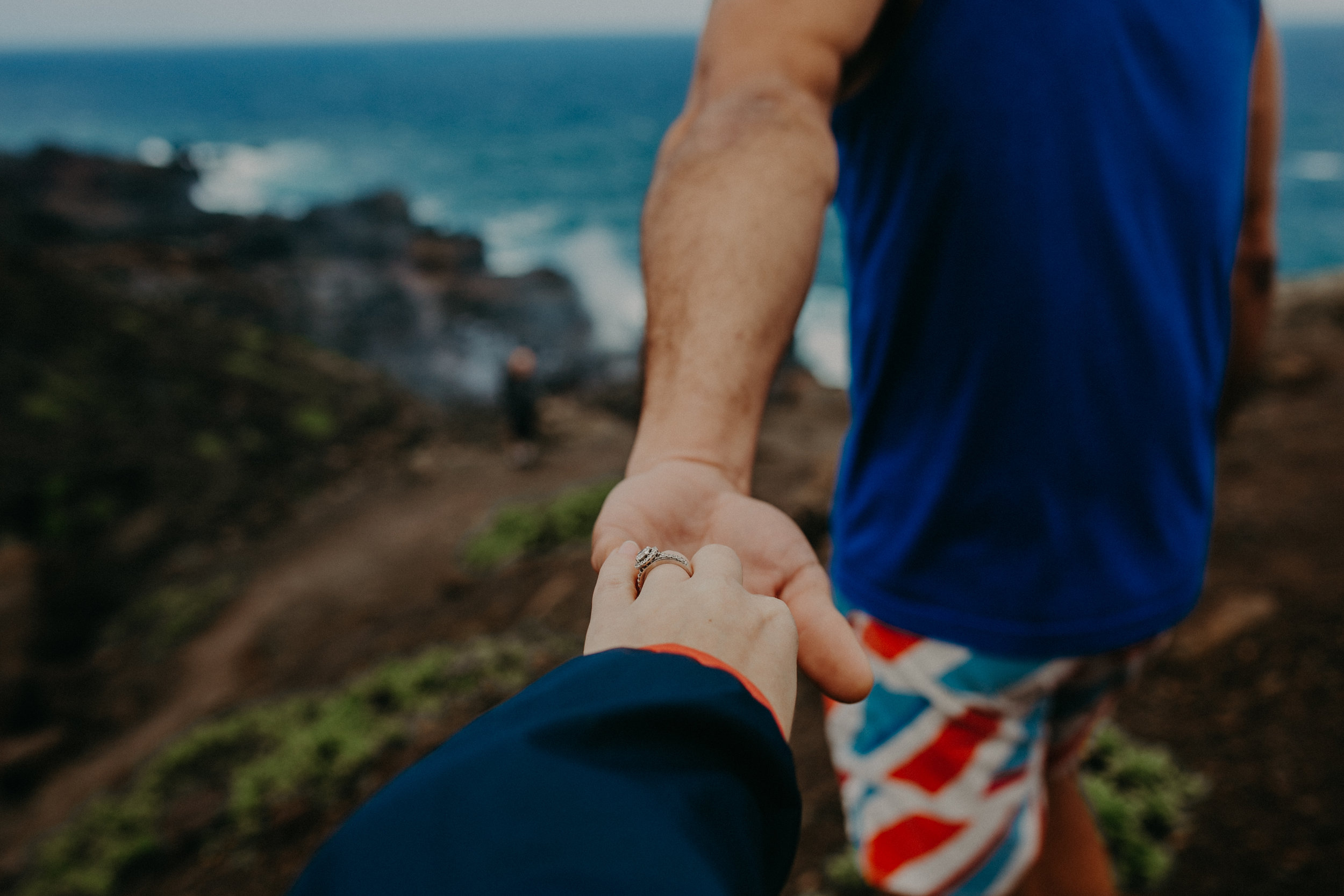 a man takes his wife’s hand while hiking along the cliffs of western Maui near the Nakelele Blowhole