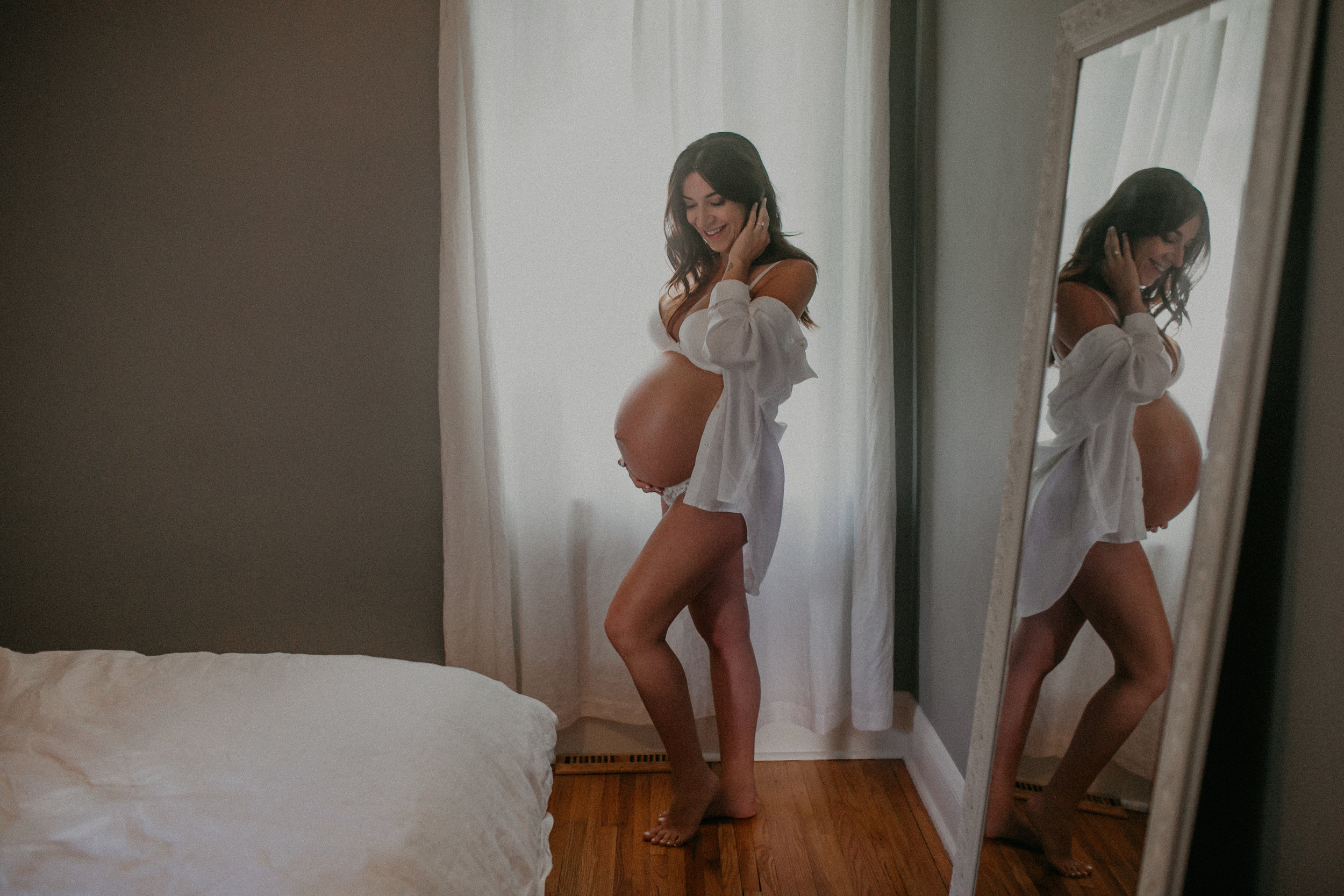 a woman poses seeing her reflection of her pregnant belly during her maternity session in Minneapolis MN
