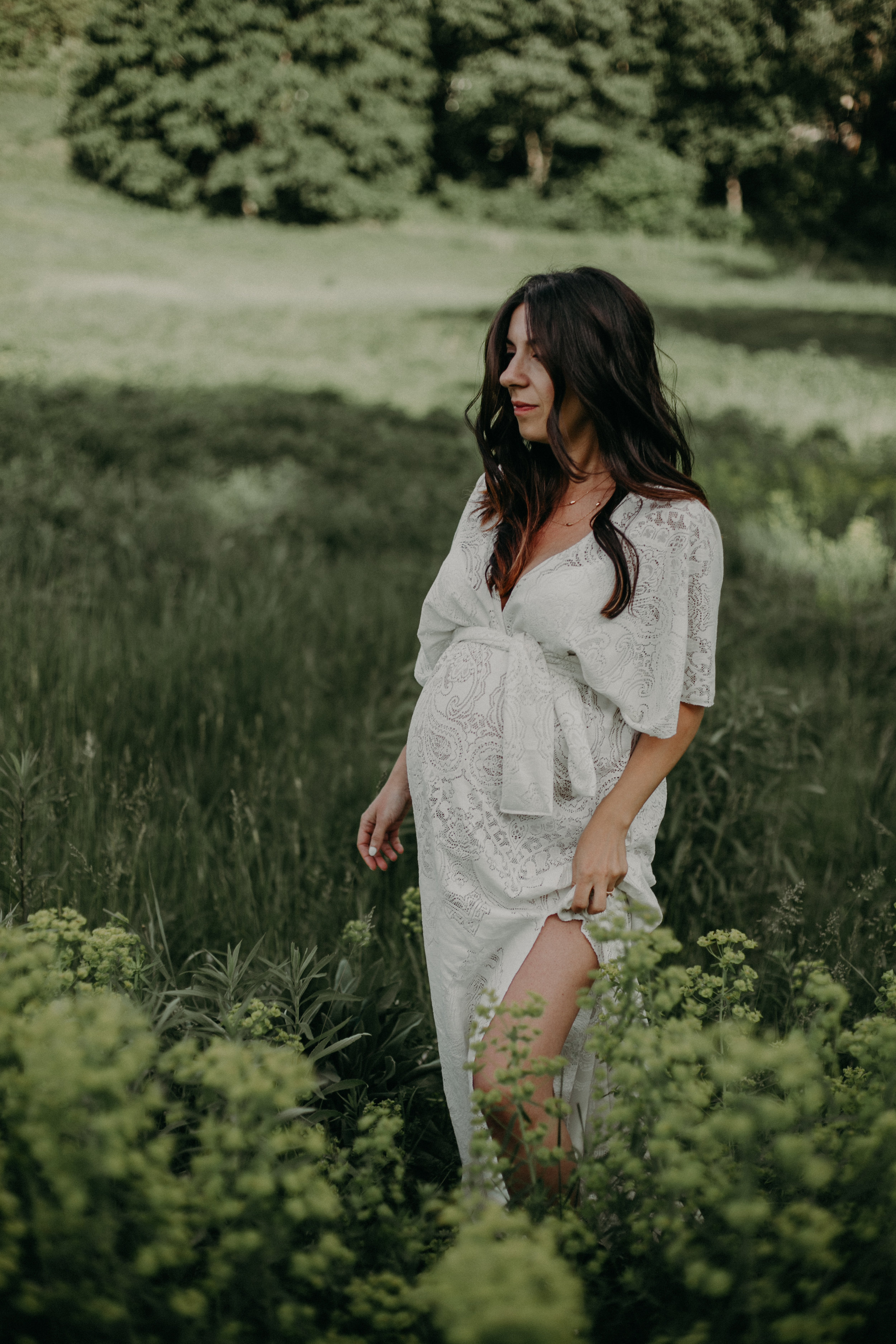  woman wears a lace white dress during her maternity photos in a Minneapolis park 