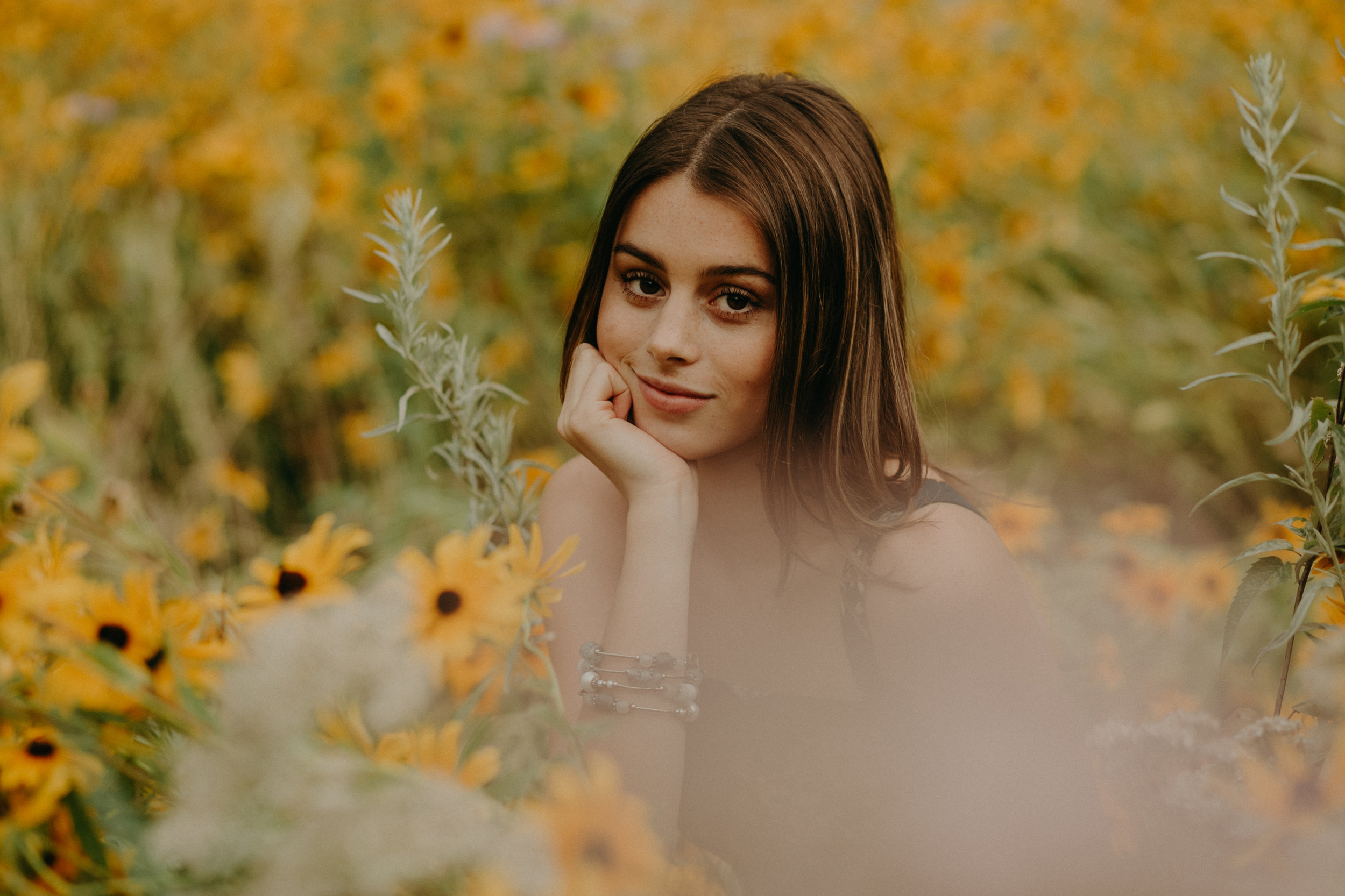  gorgeous high school senior sits in a field of yellow daisies in Minneapolis MN 