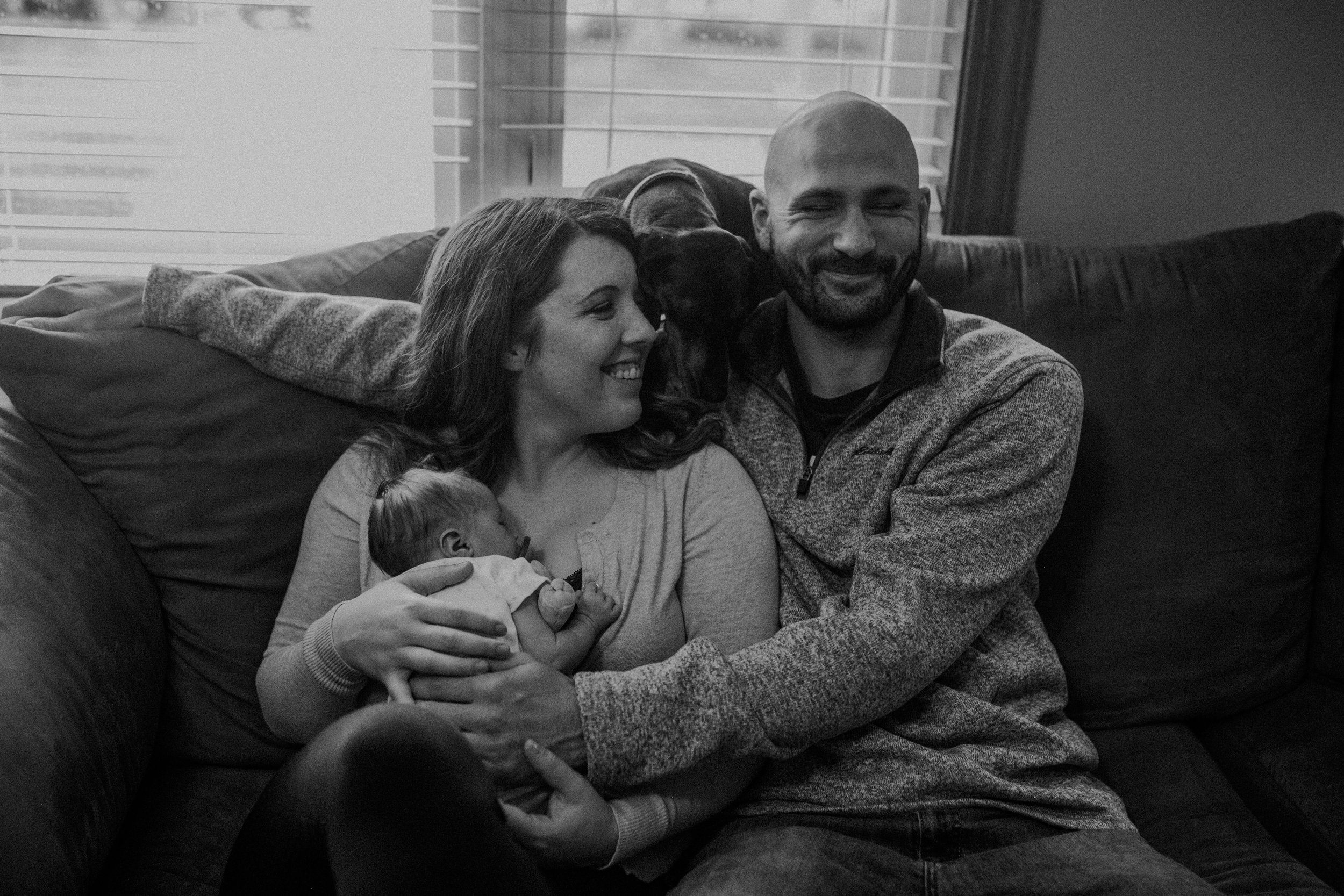  an Eagan MN couple sits on the couch laughing during their newborn photo session with Andrea Wagner Photography 