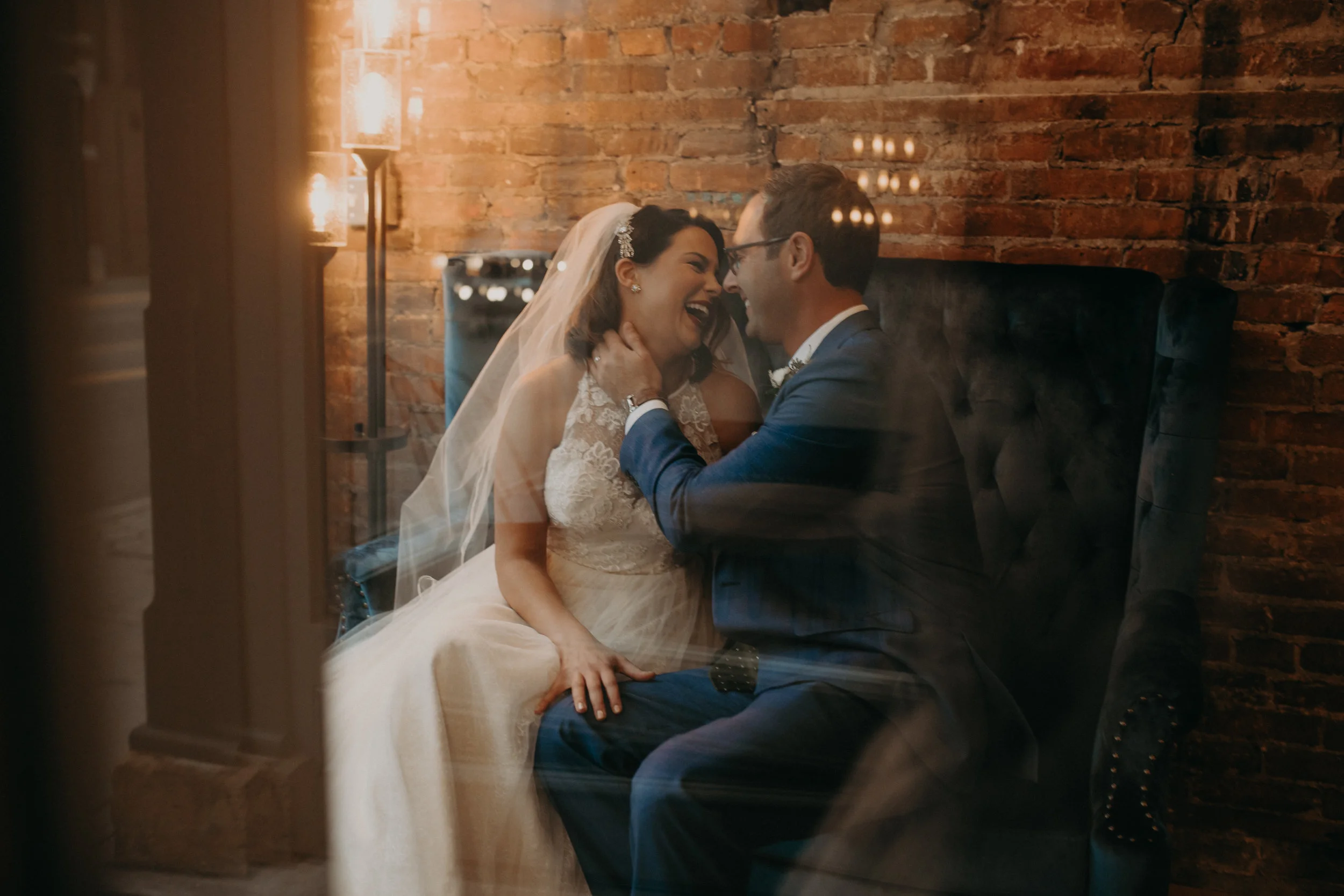 bride and groom laugh and kiss in the window of The Loft at Studio J in Stillwater MN captured by AWP