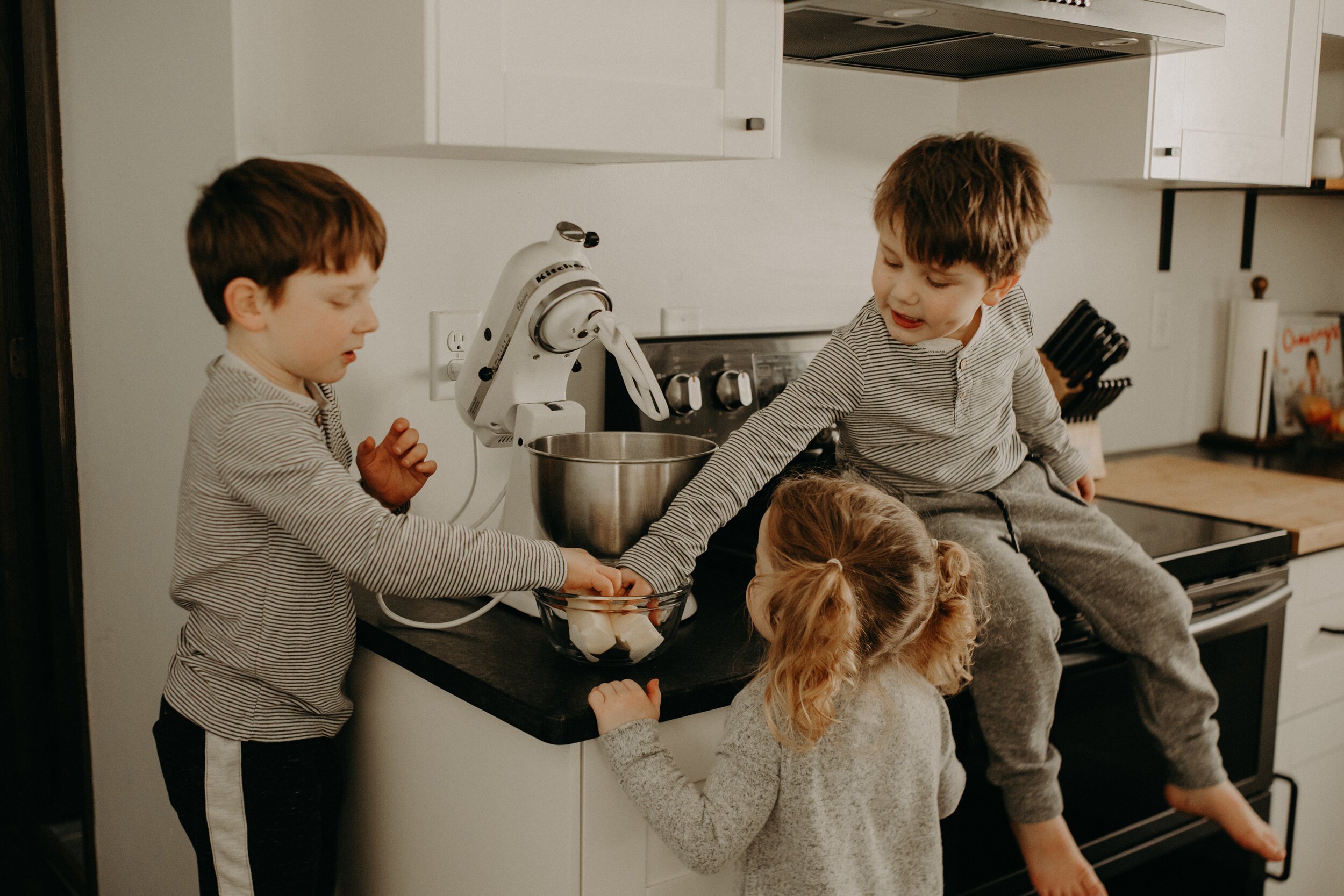  River Falls Family. River Falls Wisconsin. Mother cooking in the kitchen. Lifestyle Newborn Photo session. Wisconsin Newborn Photographer. Wisconsin Lifestyle Newborn Photographer. Lifestyle Newborn In Home Session. Beautiful mom in white making cho