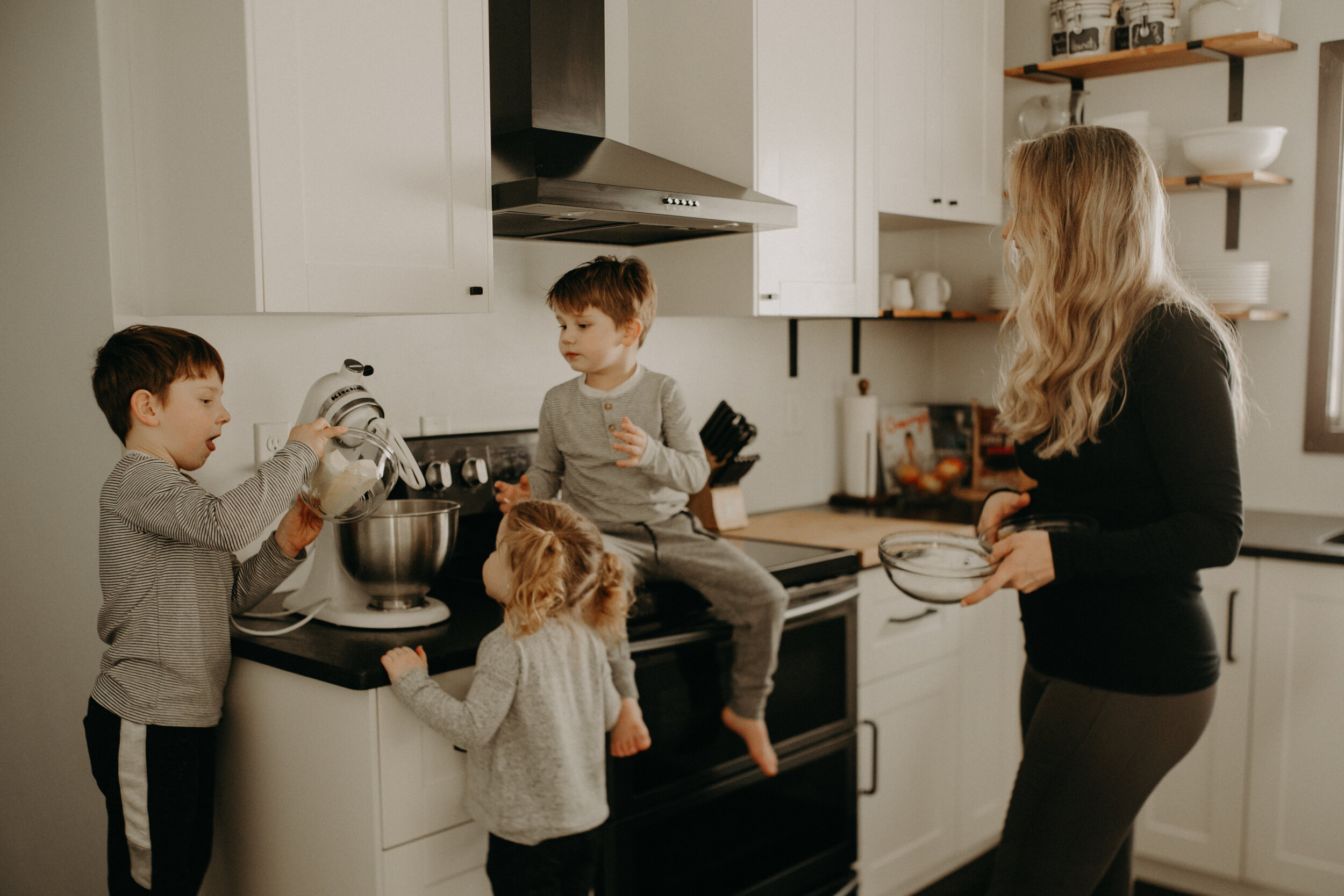  River Falls Family. River Falls Wisconsin. Mother cooking in the kitchen. Lifestyle Newborn Photo session. Wisconsin Newborn Photographer. Wisconsin Lifestyle Newborn Photographer. Lifestyle Newborn In Home Session. Beautiful mom in white making cho