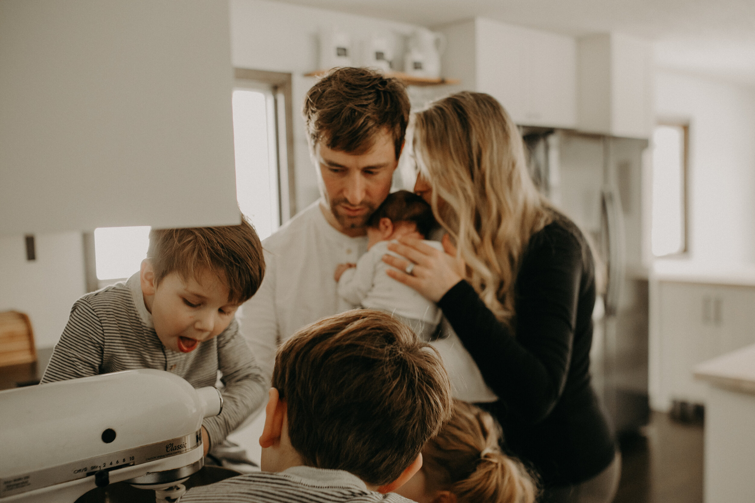  River Falls Family. River Falls Wisconsin. Mother cooking in the kitchen. Lifestyle Newborn Photo session. Wisconsin Newborn Photographer. Wisconsin Lifestyle Newborn Photographer. Lifestyle Newborn In Home Session. Beautiful mom in white making cho