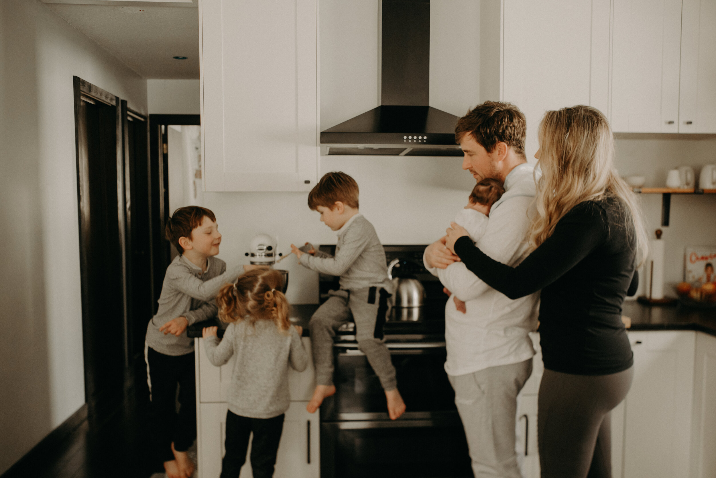  River Falls Family. River Falls Wisconsin. Mother cooking in the kitchen. Lifestyle Newborn Photo session. Wisconsin Newborn Photographer. Wisconsin Lifestyle Newborn Photographer. Lifestyle Newborn In Home Session. Beautiful mom in white making cho