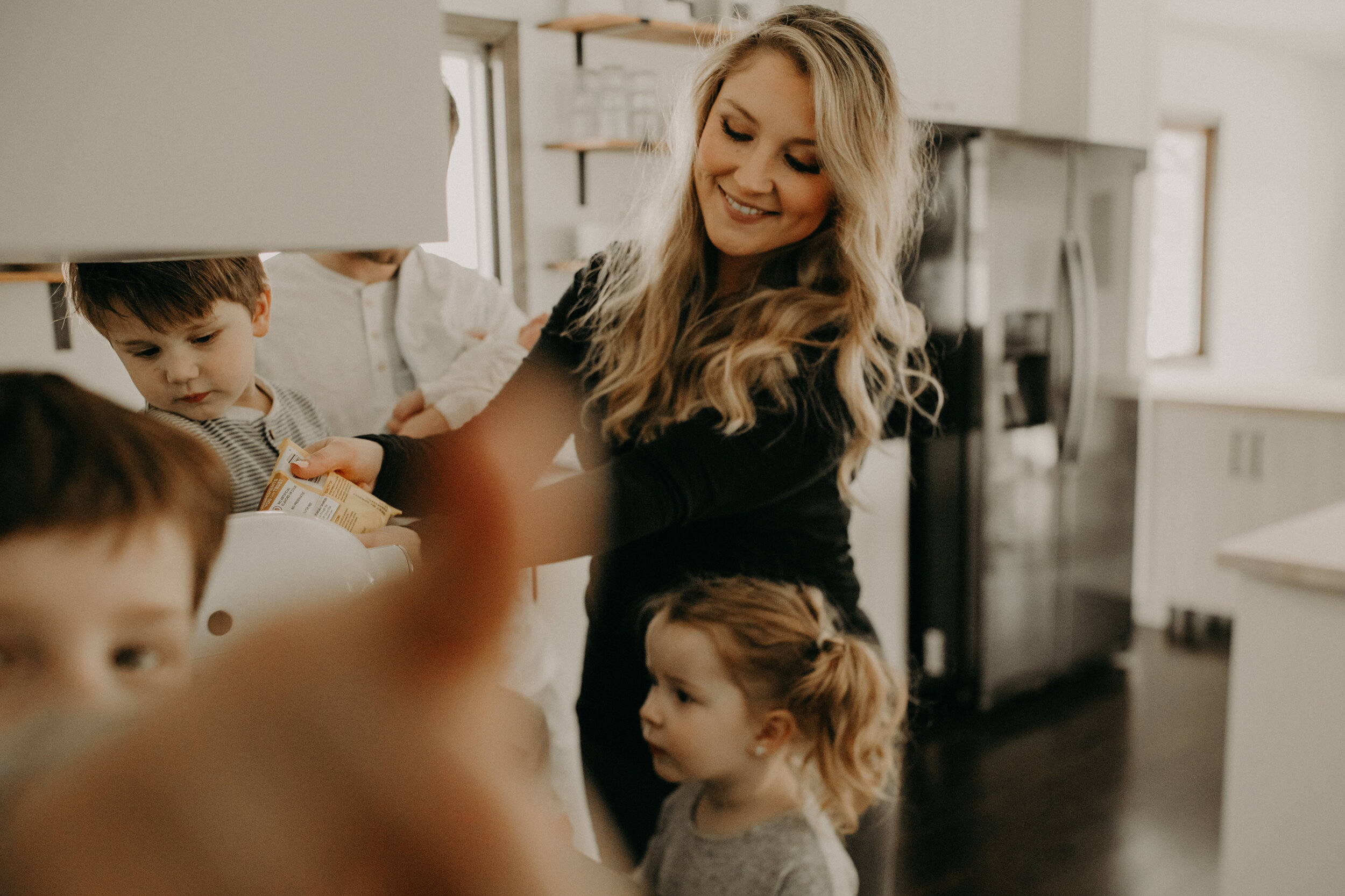  River Falls Family. River Falls Wisconsin. Mother cooking in the kitchen. Lifestyle Newborn Photo session. Wisconsin Newborn Photographer. Wisconsin Lifestyle Newborn Photographer. Lifestyle Newborn In Home Session. Beautiful mom in white making cho