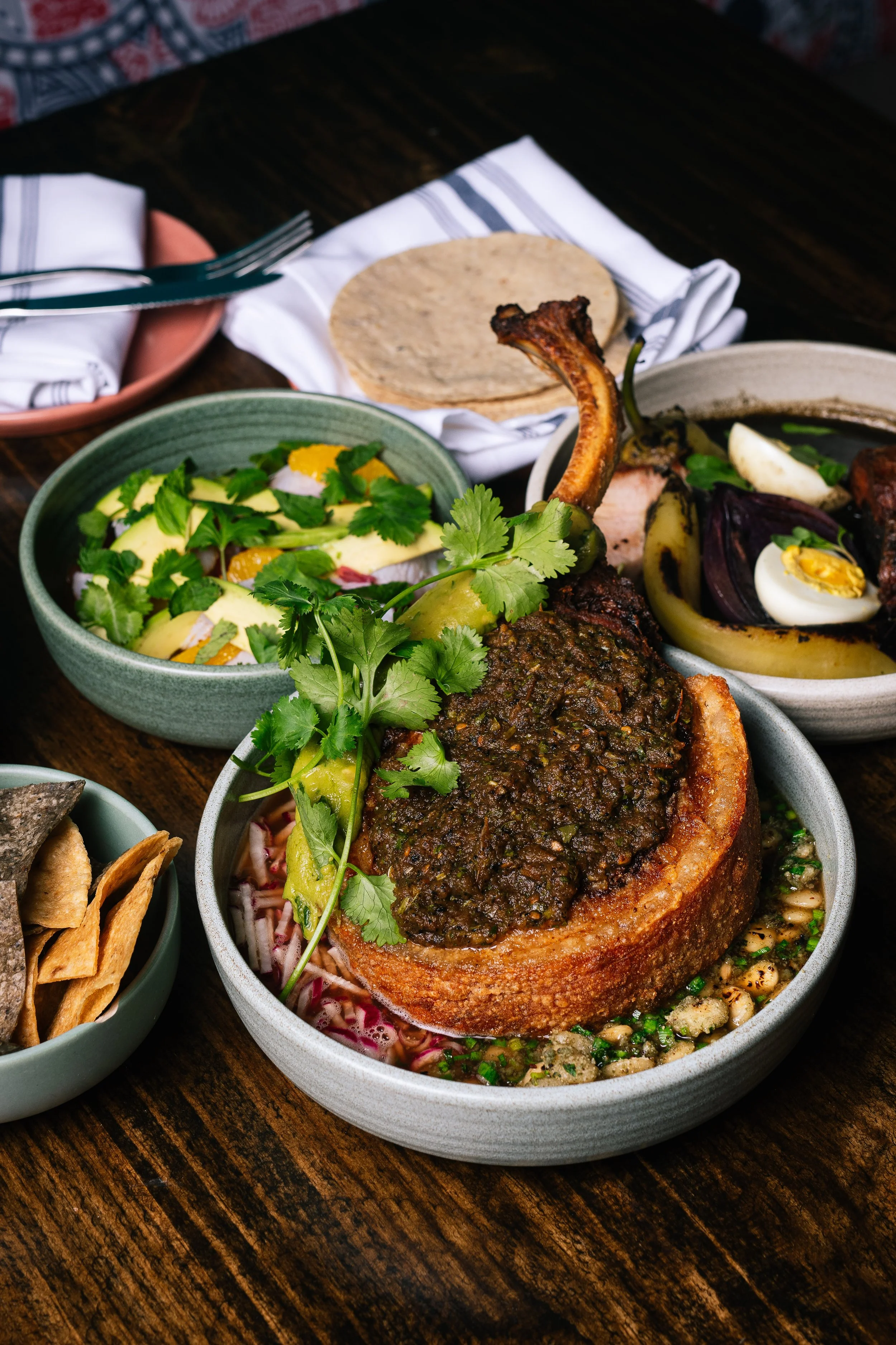 A table with various Mexican dishes, including a bowl with a piece of pork with mole sauce, a bowl with a salad, and a bowl with roasted vegetables and eggs.