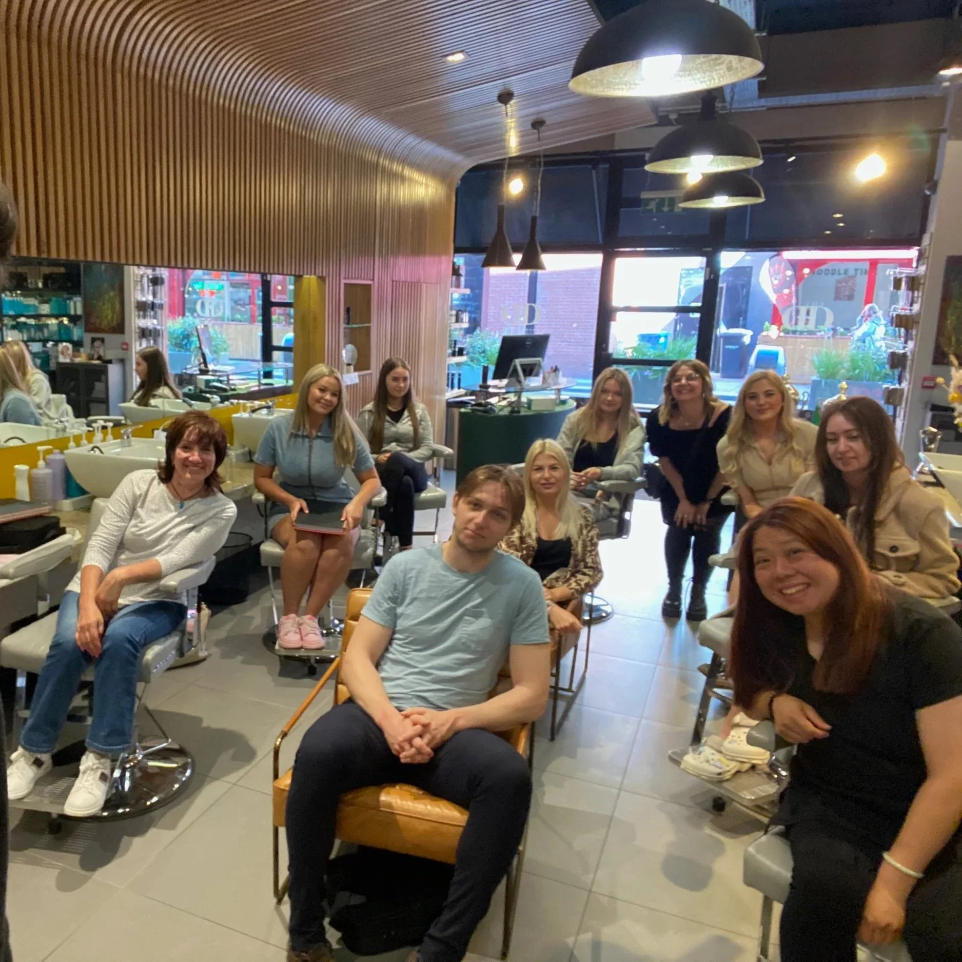 A group of people sitting and standing inside a modern hair salon enjoying the hairdressing live subscription