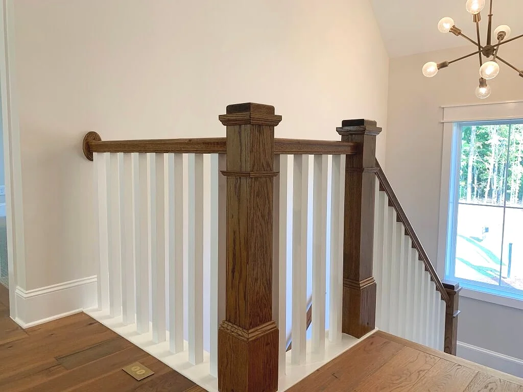 Farmhouse style traditional stairway with square painted spindles and mission style stained wood posts.