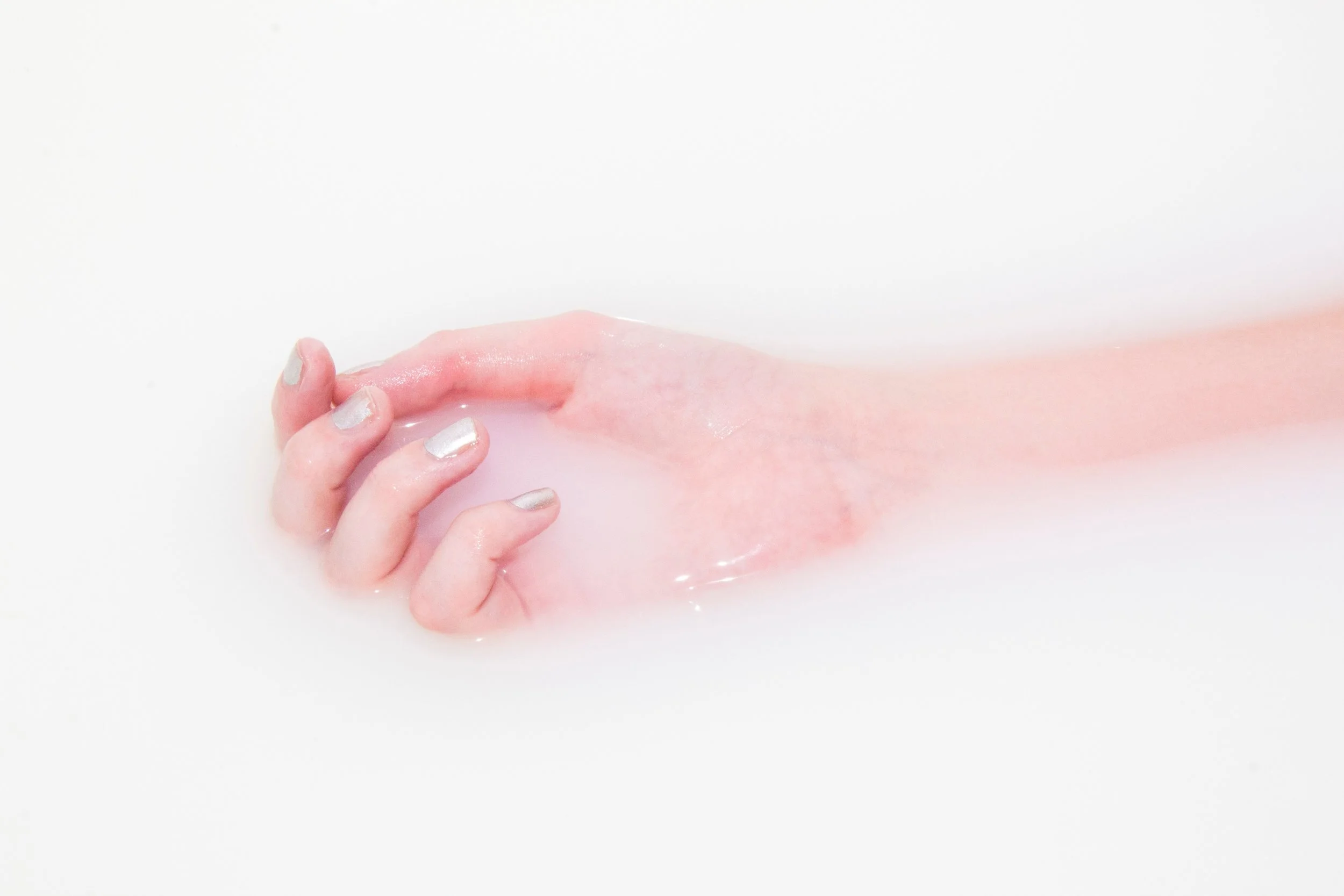 A hand with light colored polish lays in a bath of milky water.