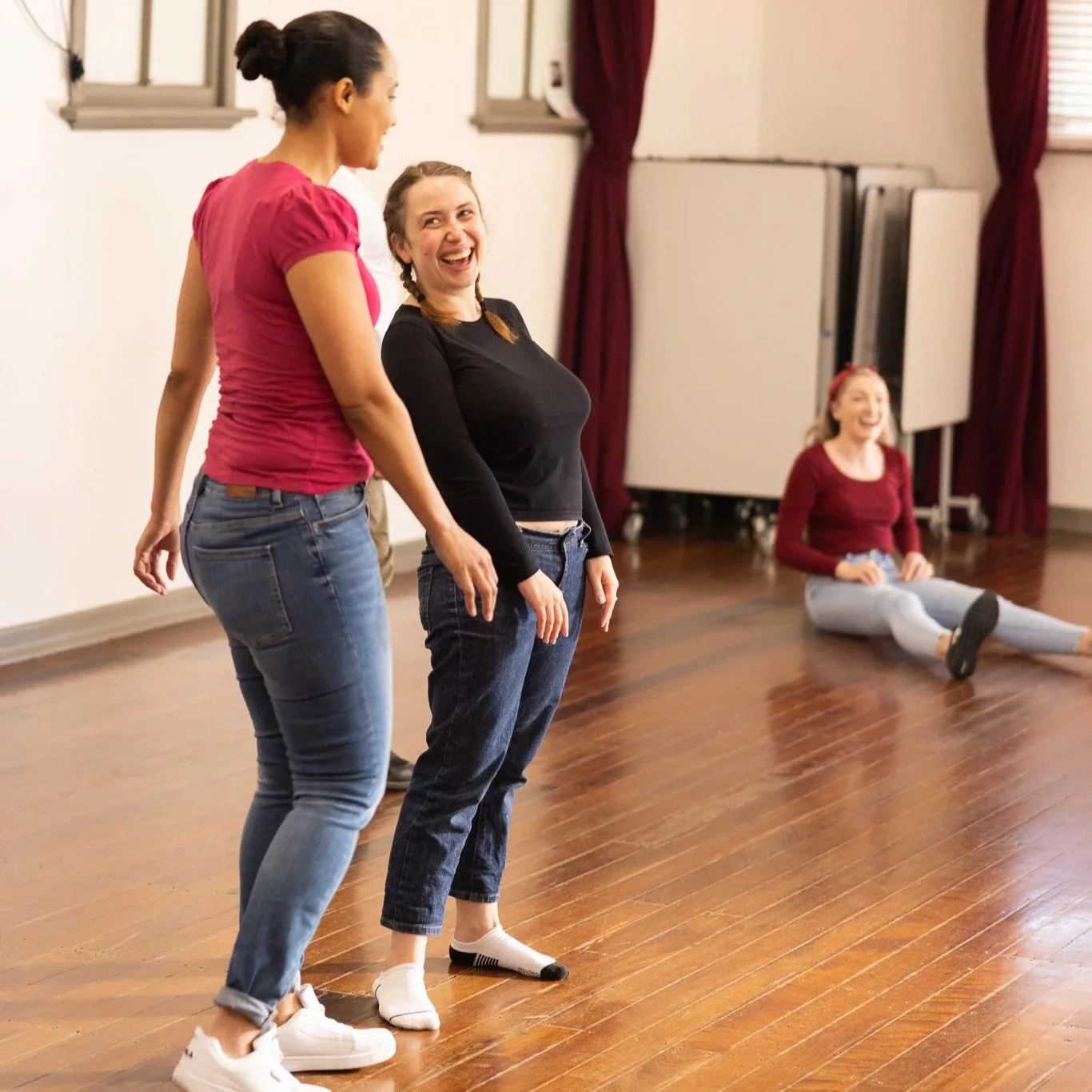 Two people laughing in an improv class while a third laughs on the floor