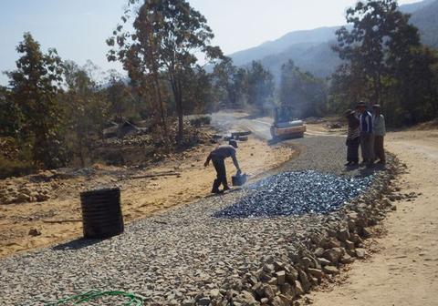 The bitumen being laid over the rocks from perforated kerosene tine, prior to rolling.