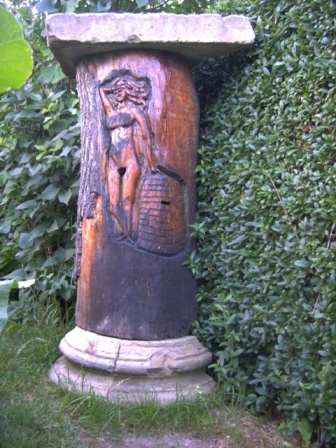 A Carved Klotzbeute – no longer containing bees, but used as a garden ornament. The lighter lid on top, which could be removed to inspect the hive, has been replaced by a heavier concrete lid.