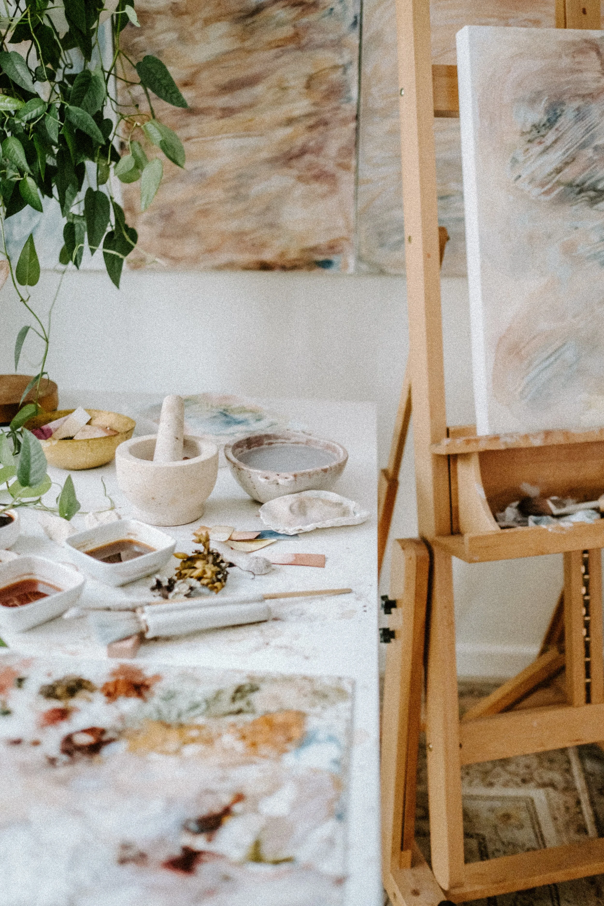 Art studio with painting supplies, easel, canvas, plants, and dried flowers on a table.