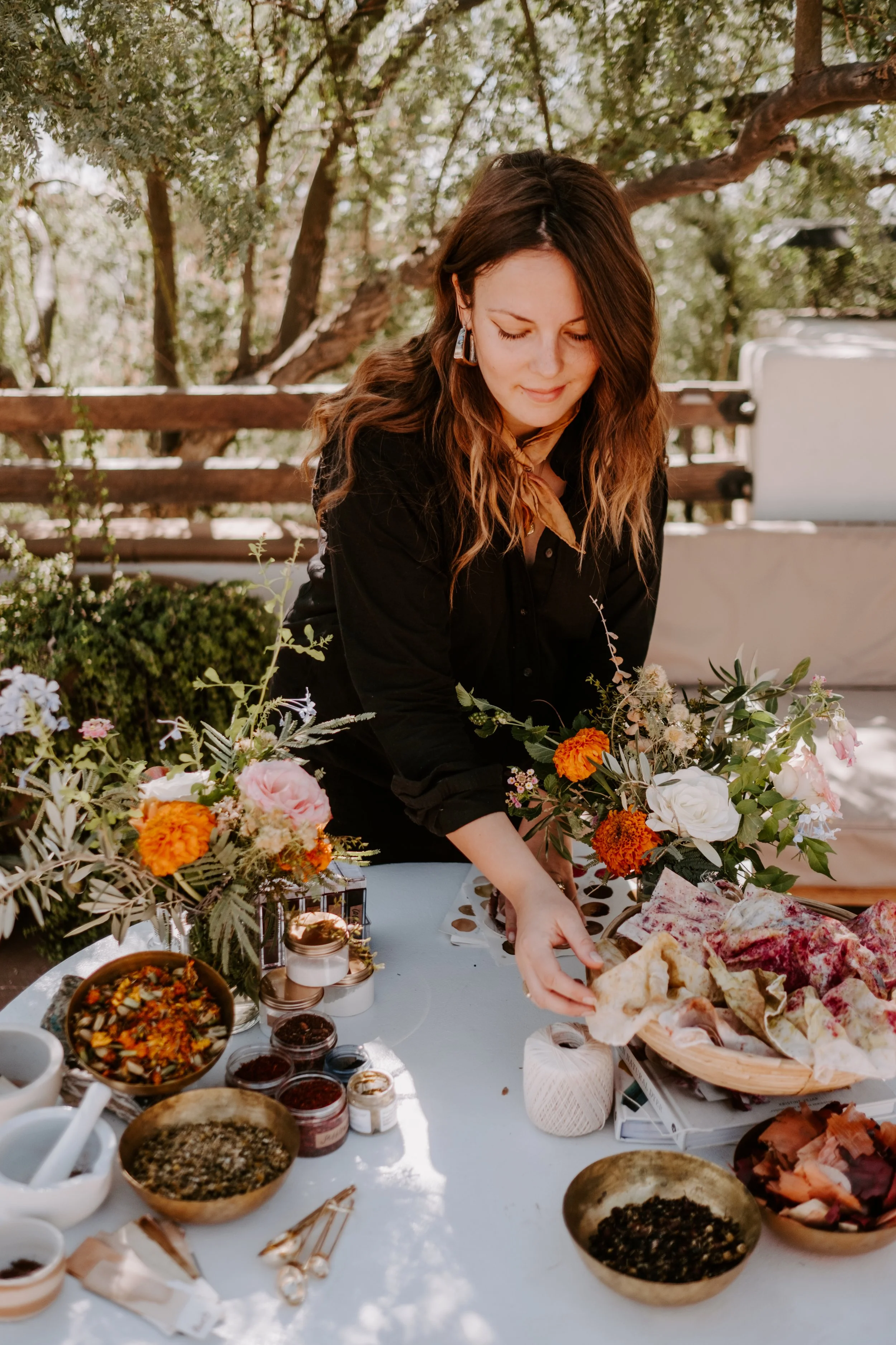 Woman arranging flowers and food on a table outdoors.