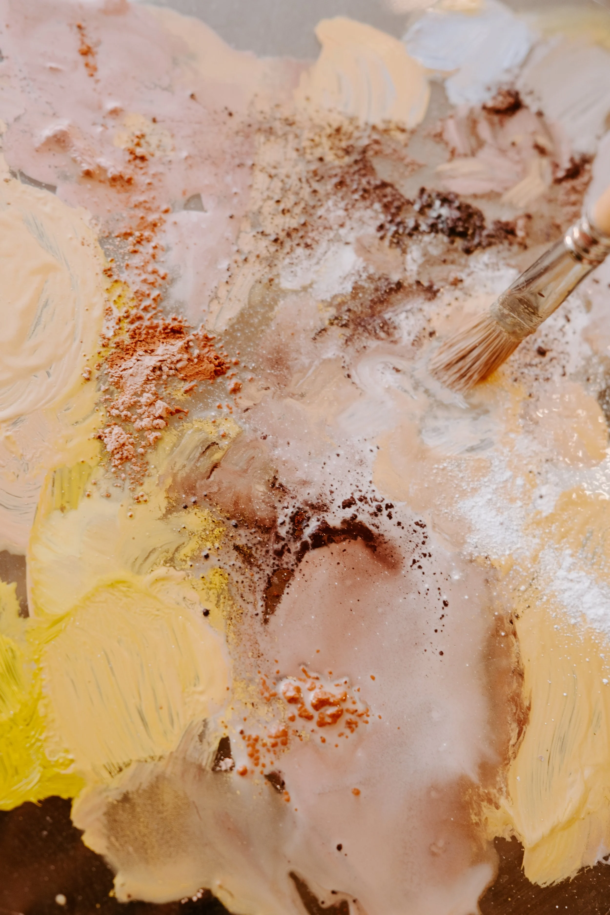 Close-up of a paintbrush mixing various colors and textures on a palette.