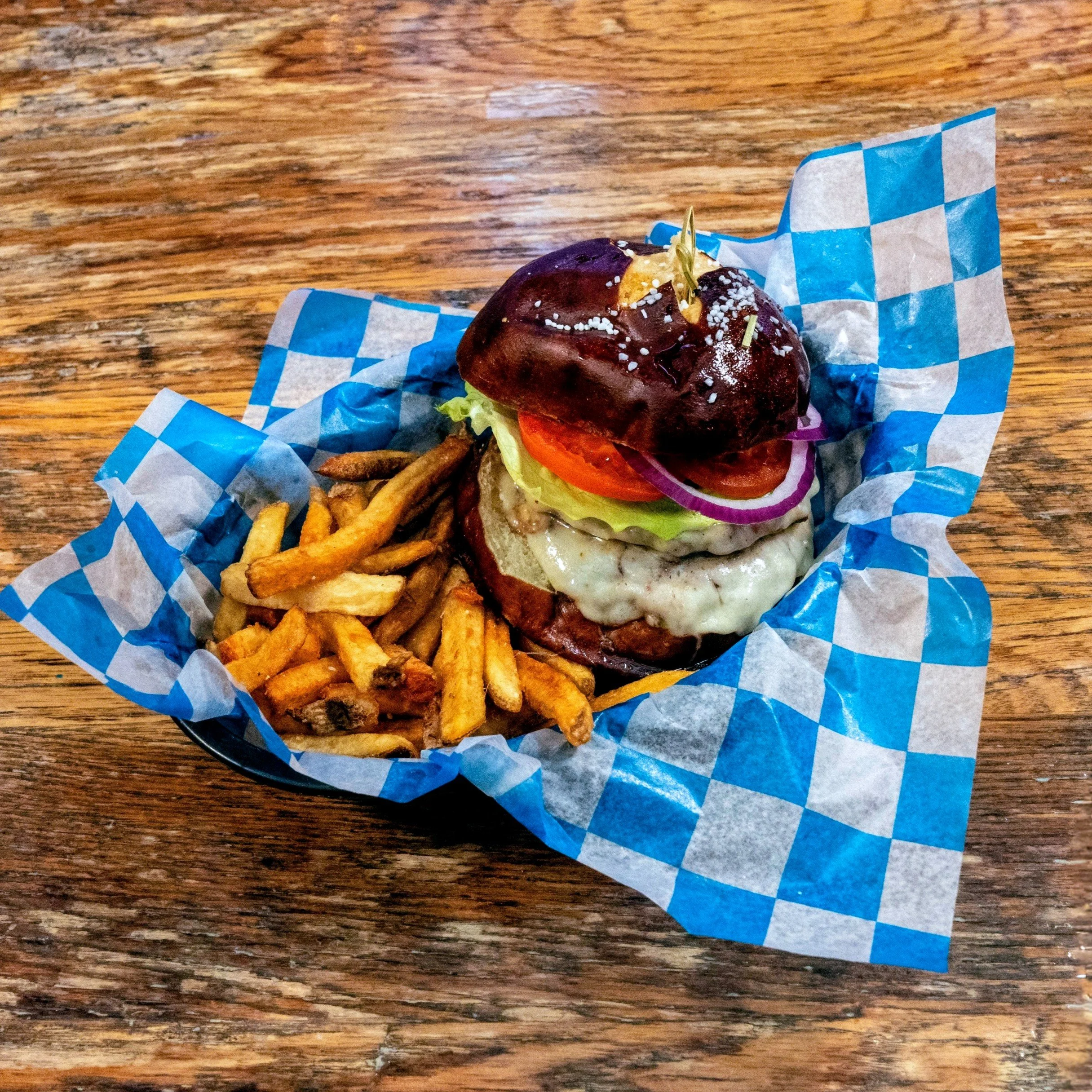 Two patty burger with muenster cheese on a pretzel bun with lettuce, tomato, onion.