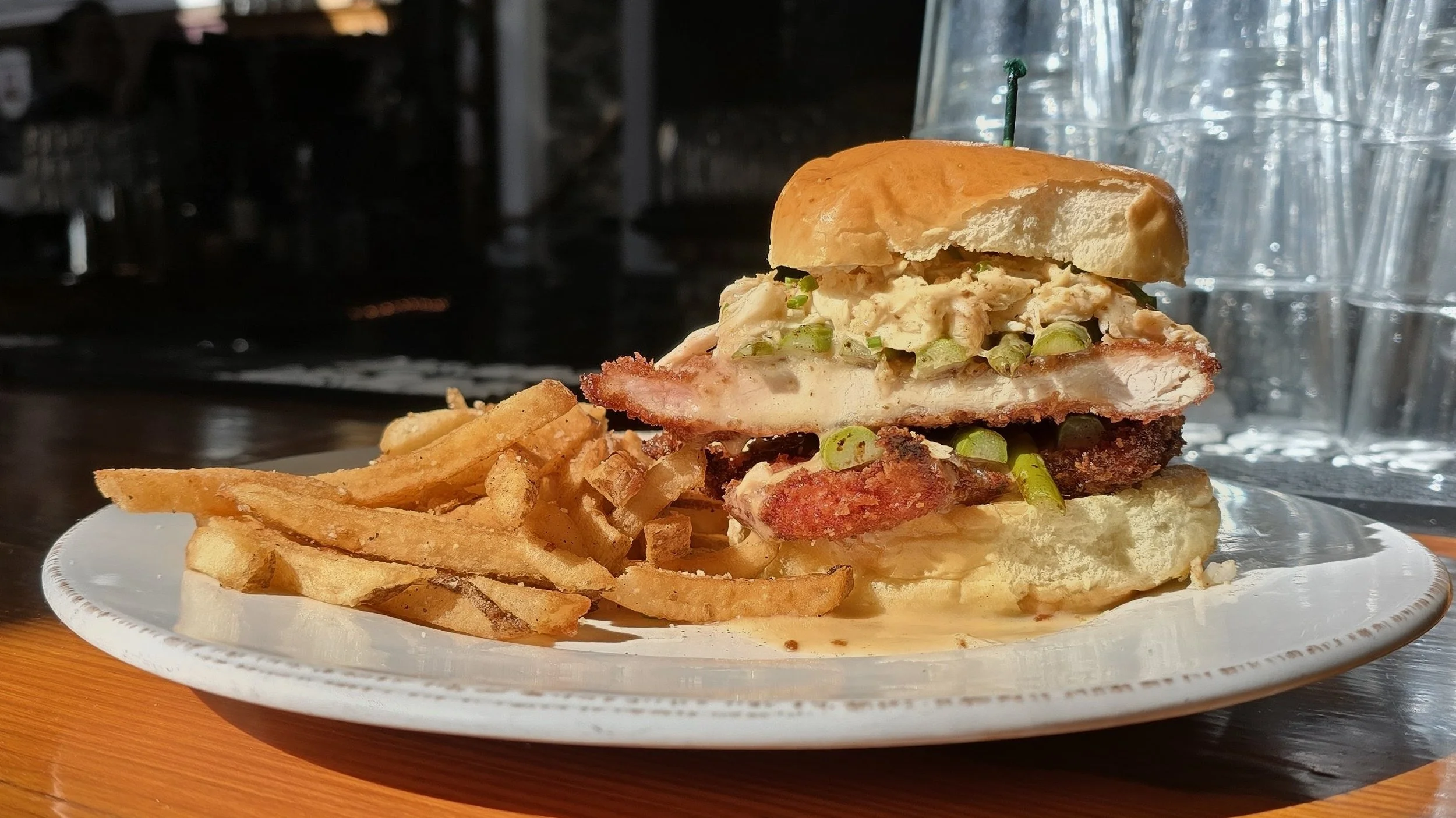 Chicken schnitzel topped with crab and lemon beurre blanc sauce, asparagus, on a white bun.