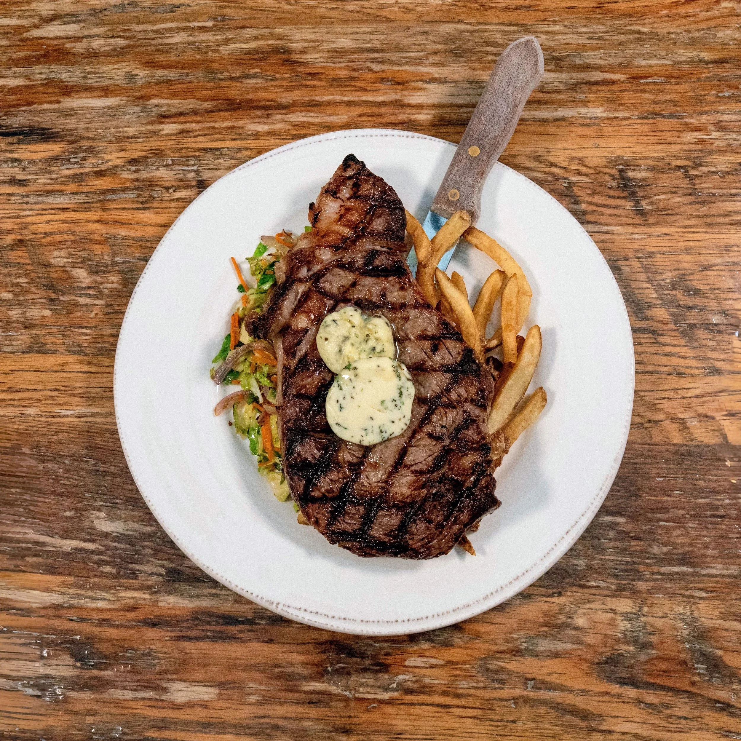 Grilled ribeye with compound herb butter, frittes, and mixed vegetables.