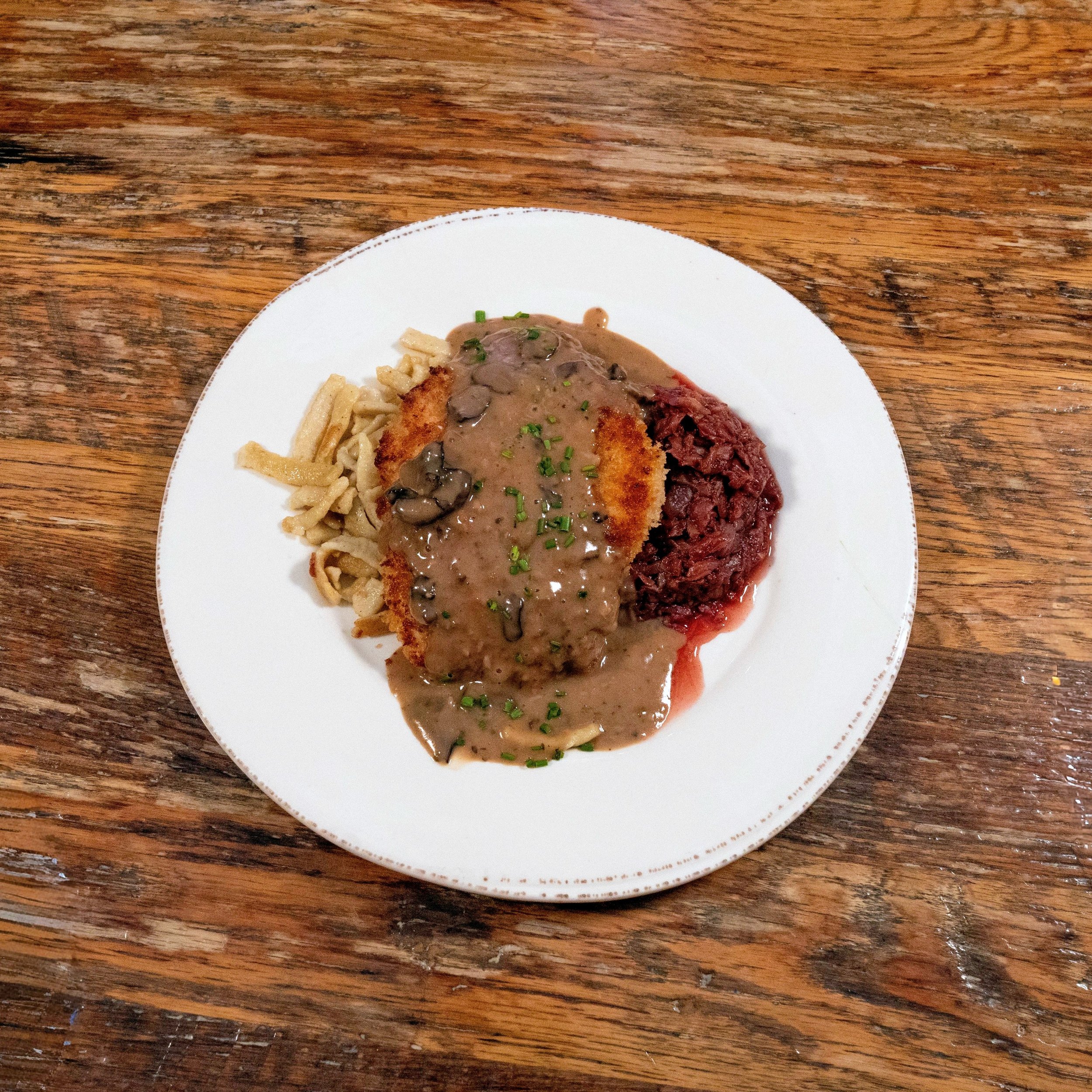 Chicken Schnitzel topped with jager hunter mushroom gravy sauce, served over red cabbage and spatzle.