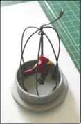 step 12 - Put a wire under the center top of all the cage wires and the swing wire and twist it to secure them together. Leave a long tail on the wire to use as a hanger for the ornament. straighten the cage wires if needed. Glue rhinestones around the textured ring.
