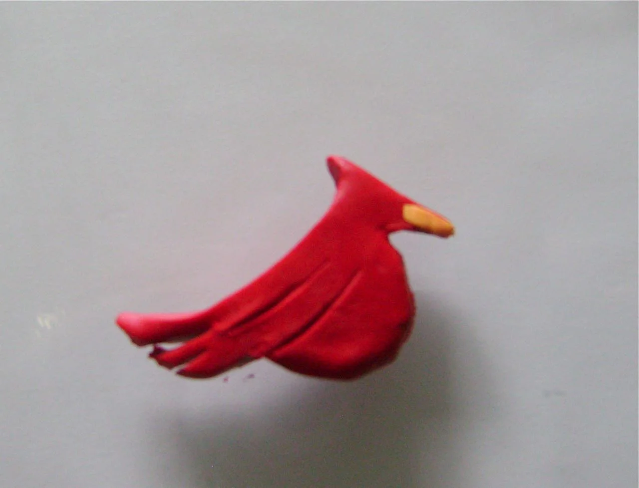 step 8 - Roll a small piece of yellow clay between your fingers and flatten. Place it over the birds beak covering the red clay.