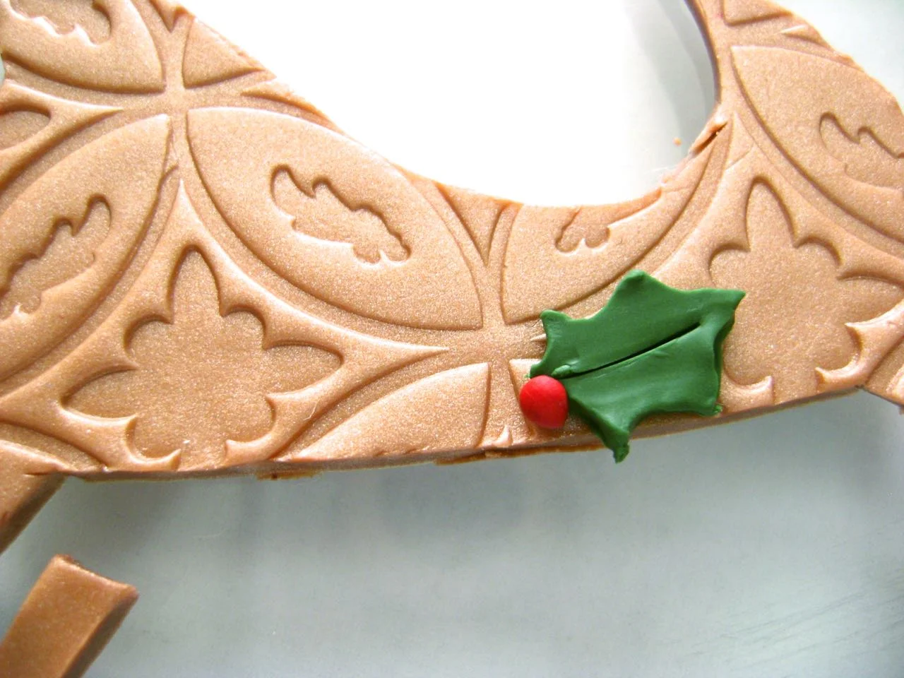 step 5 - Condition and roll out a small piece of green clay and a tiny piece of red clay. Cover the green clay with plastic wrap then cut out two small holly leaves with the craft knife. Roll three tiny pieces of red clay between your fingers to create the berries. Position the holly and berries at the bottom of the sleigh.