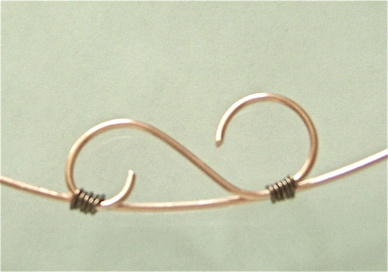 step 9 - Use 22 gauge copper wire to wrap the decorative “S” shape to the center of the runner wire. Hold the pieces together and wrap the thin wire around them 4 times. Cut off the excess.