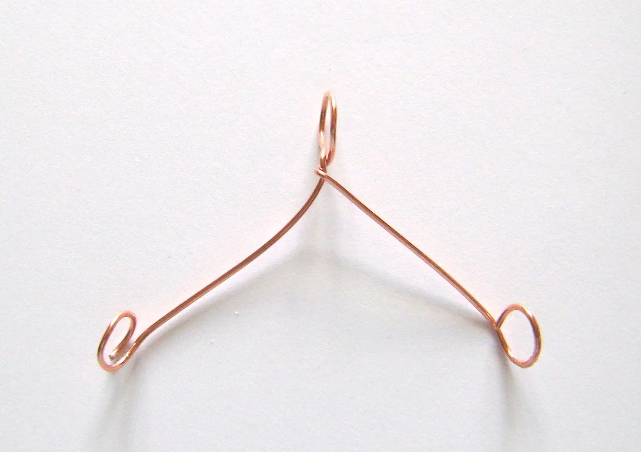 step 13 - Create a hanger for the sleigh with about 6” of 18 gauge wire. Bend the wire in half over a round object. Twist the long ends once to wrap them and create a center loop. Create loops on the wire ends. Both loops should be the same distance from the center so the sleigh will hang straight. Bend the loops to face each other and slip one curl of the sleigh into each.