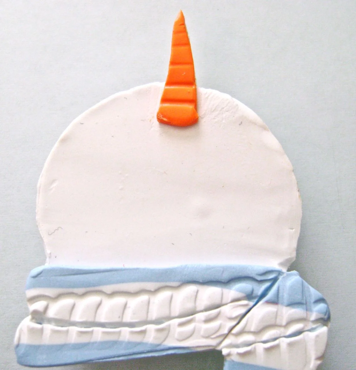 step 6 - Use the Etch n’ Pearl tool to create fold creases in the scarf. Use the snowman template to cut the shape of the nose from orange clay. Place the piece on the snowman aligning the edges. Note that the nose should extend down on the face about the same distance as it extends up.