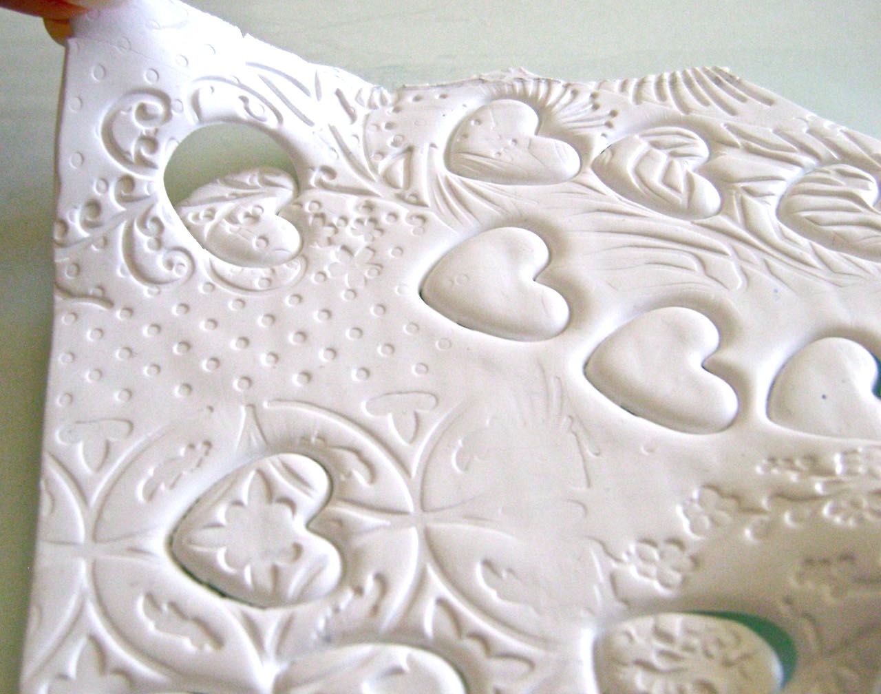 step 5 - Lift the clay sheet leaving the heart shapes on the work surface. Roll the sheet together, flatten and cut out more hearts if necessary. Cut the heart frames using a mini heart cutter centered inside the hearts you just made. Don’t forget to put down the plastic wrap.