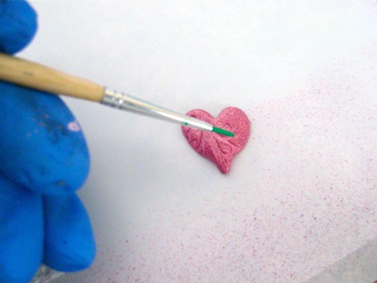 step 11 - Create contrasts to bring out the small details in the surface of the pink and mauve hearts. In a small container, water down a little of the green color. Use a small brush to apply it across the hearts being sure it seeps into the impressions. Immediately dab at the paint with a rag to remove most of the wet paint leaving color in the impressions. 