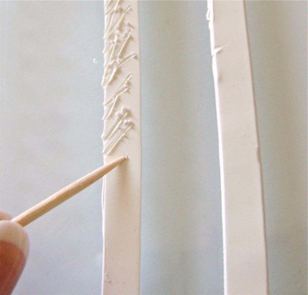 step 12 - With a blade, cut a 3/8” wide strip of white clay long enough to reach from the bottom left to the bottom right of the coat following the outer edge. Use a toothpick to pull at the clay creating a textured fur surface.