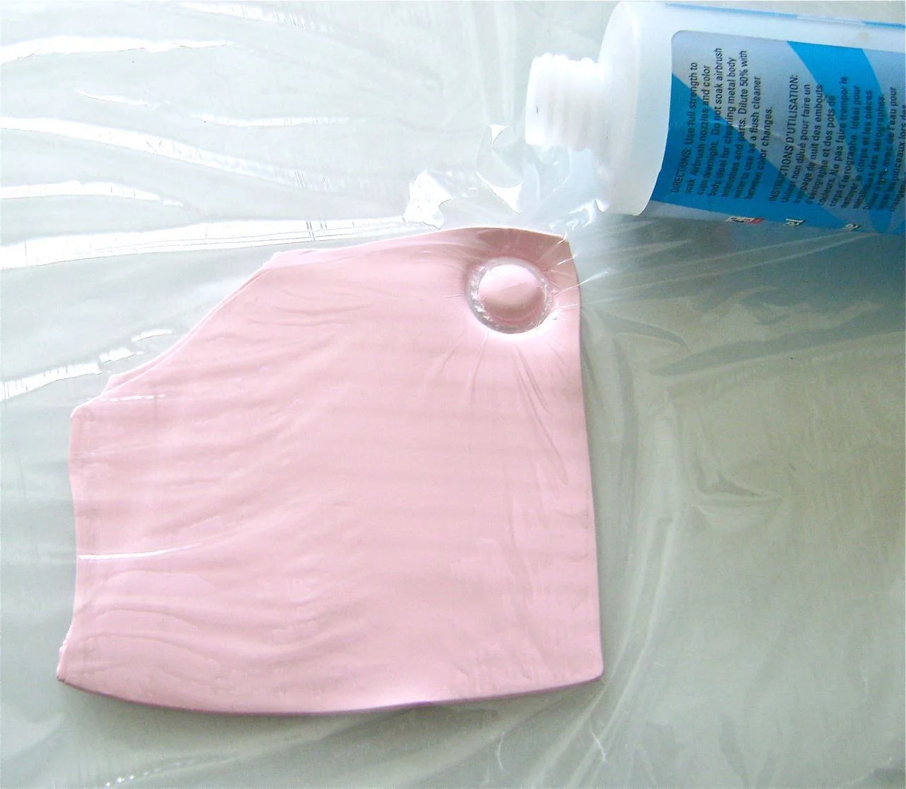 step 5 - Place the clay on wax paper. Cover it with kitchen plastic wrap. Press a circular shape into the clay that measures 3/4” or less. Bottle caps and container openings with fine edges are ideal. The size should fit into the squares on the board with a little breathing room. Cut 12 white circles and 12 pink.
