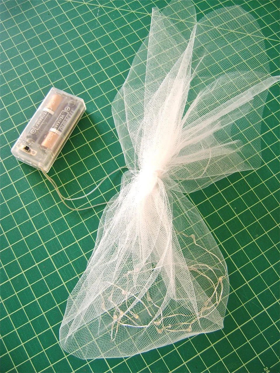 step 16 - The Lights - Cut a square of netting to measure 20". Place the lights ( not the battery pack) loosely in the square. Bring all the corners of the netting together and secure them by wrapping the fabric with thread. 
