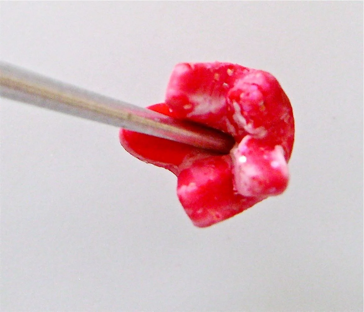 step 14 - Mix a small piece of red and white clay. Use a star cutter to create the boutonniere flower. Curve and stretch the star points up and together. Use green clay to create a stem.