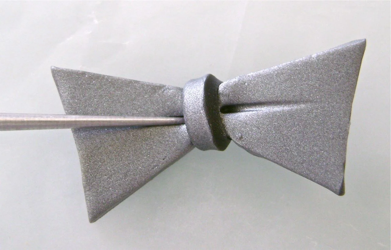step 16 - Cut a bow tie shape from the clay and wrap a thin piece around the center. Use an Etch ‘n Pearl tool to add detail.