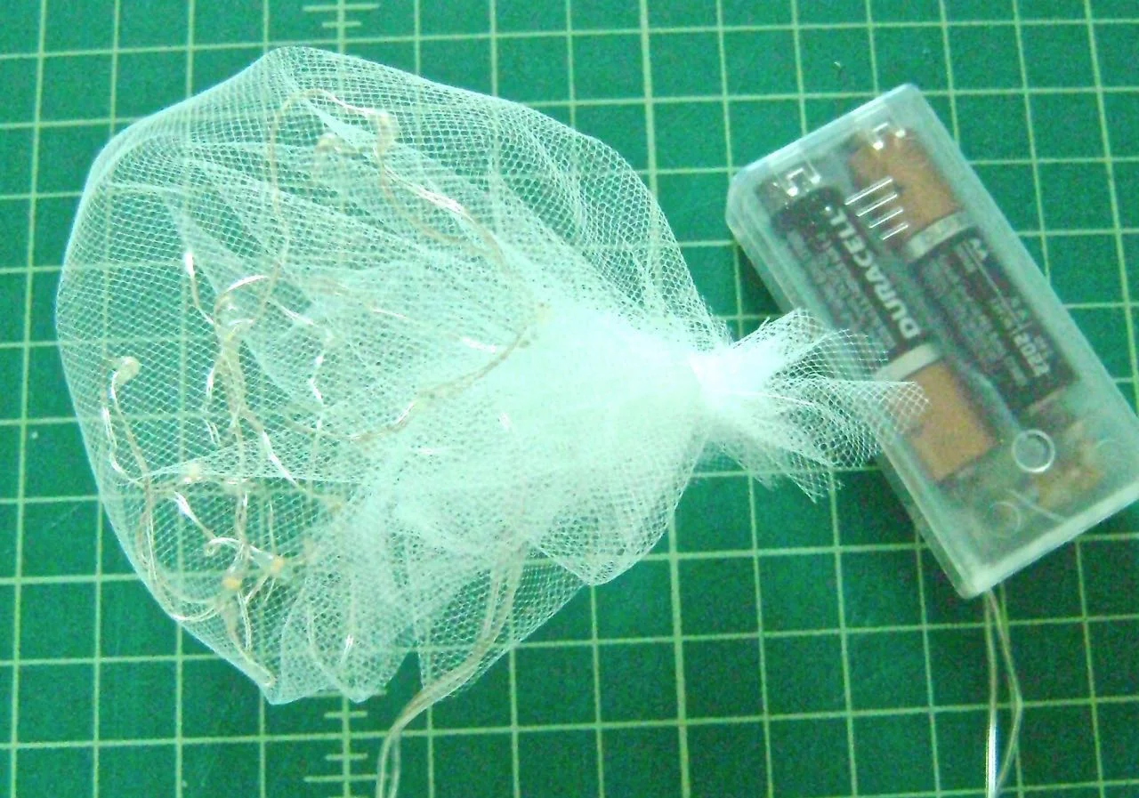 step 17 - Wrap the light string loosely in a 12” square of netting fabric and secure the ends together with string to form a pouch. Cut away excess netting. 